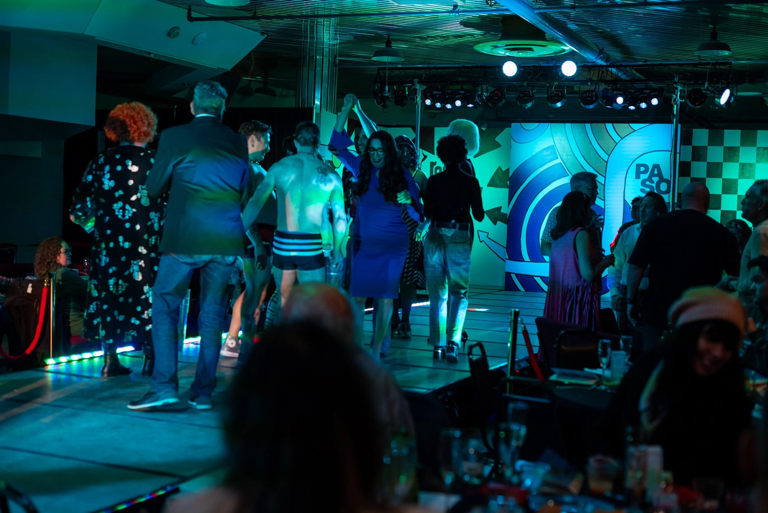 People dancing and socializing at a party or event in a dimly lit room with colorful lighting and modern decor.