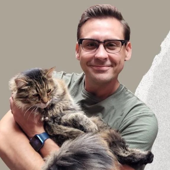 A smiling man wearing glasses holding a fluffy tabby cat.