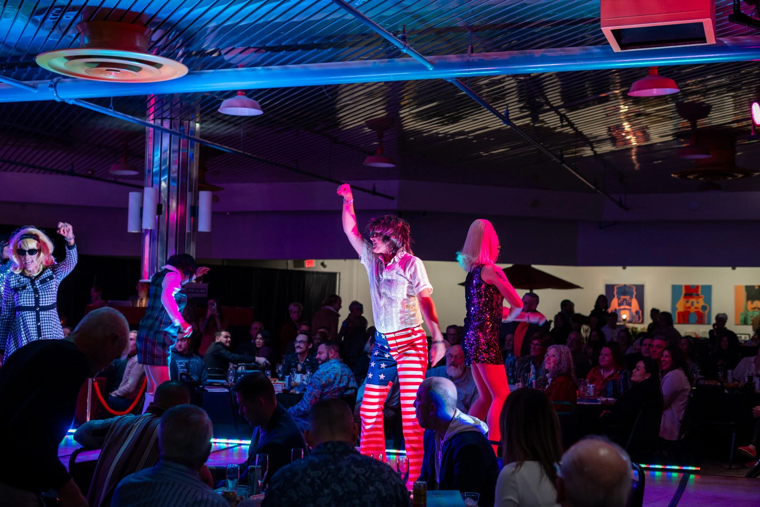 People dancing on stage with colorful lighting in a lively nightclub or event venue.