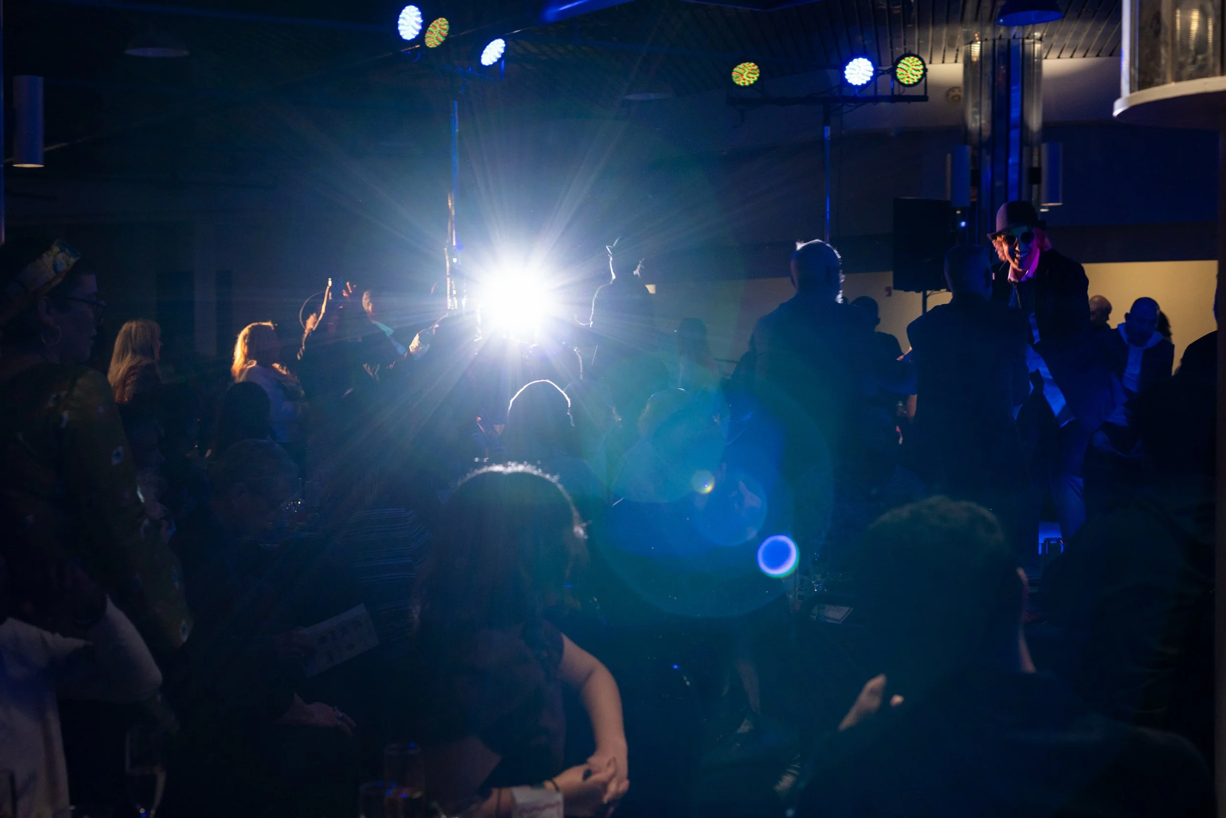 People dancing and enjoying a party or nightclub, illuminated by colorful disco lights with a bright flash of light in the background.