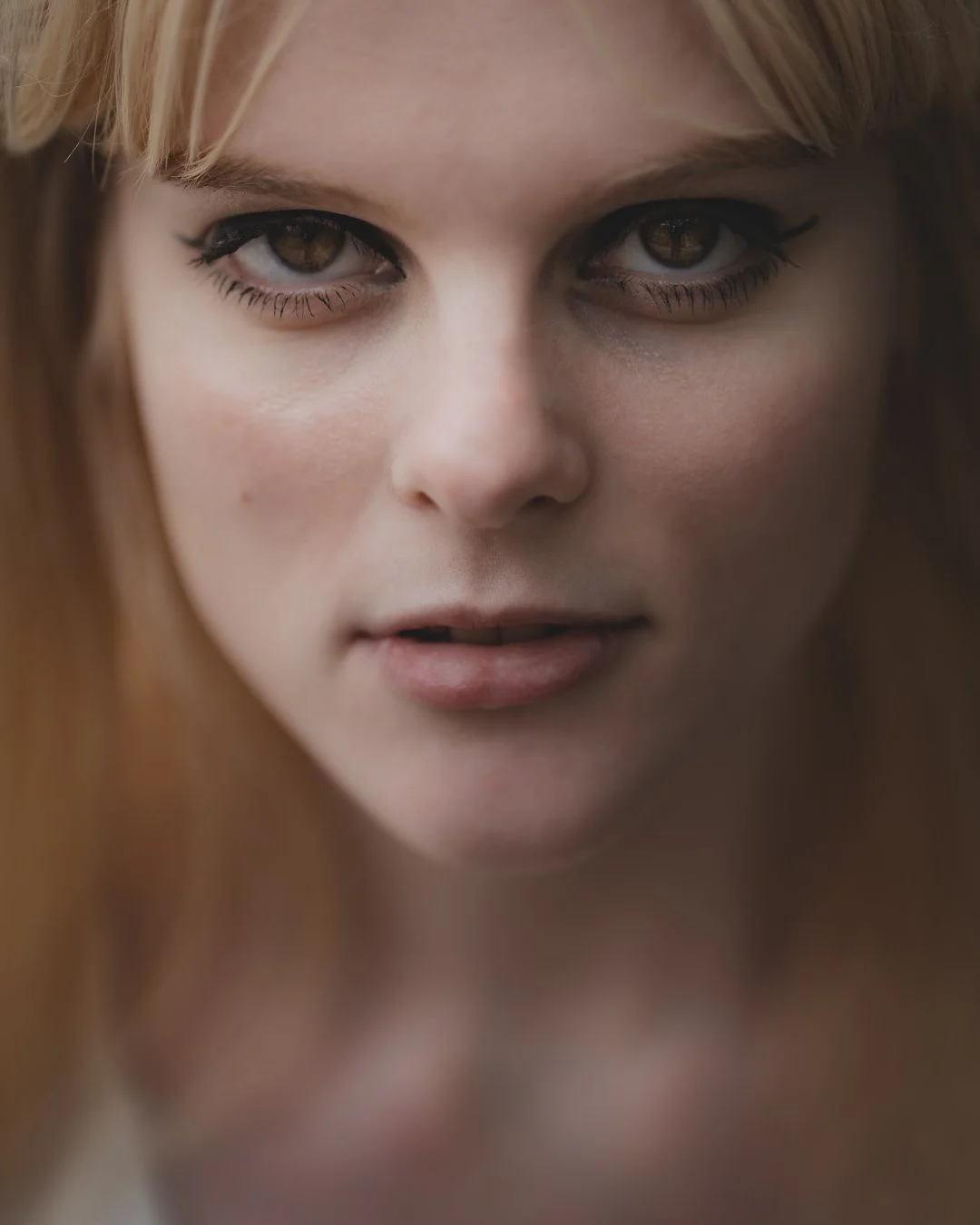 Close-up of a woman with brown eyes, light skin, red hair, and makeup, looking directly at the camera.