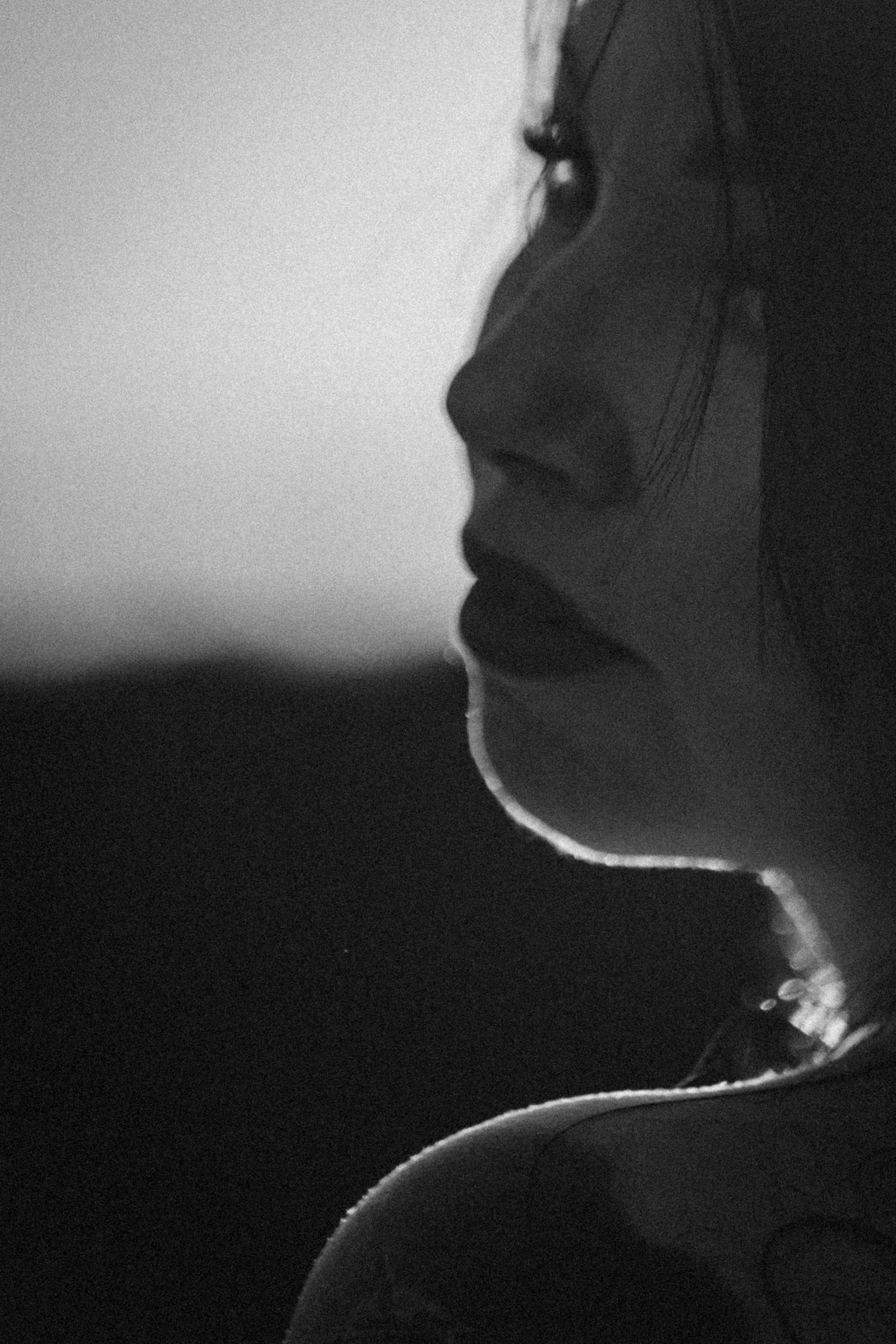 A black and white close-up portrait of a woman with long hair, looking sideways, with a neutral expression.