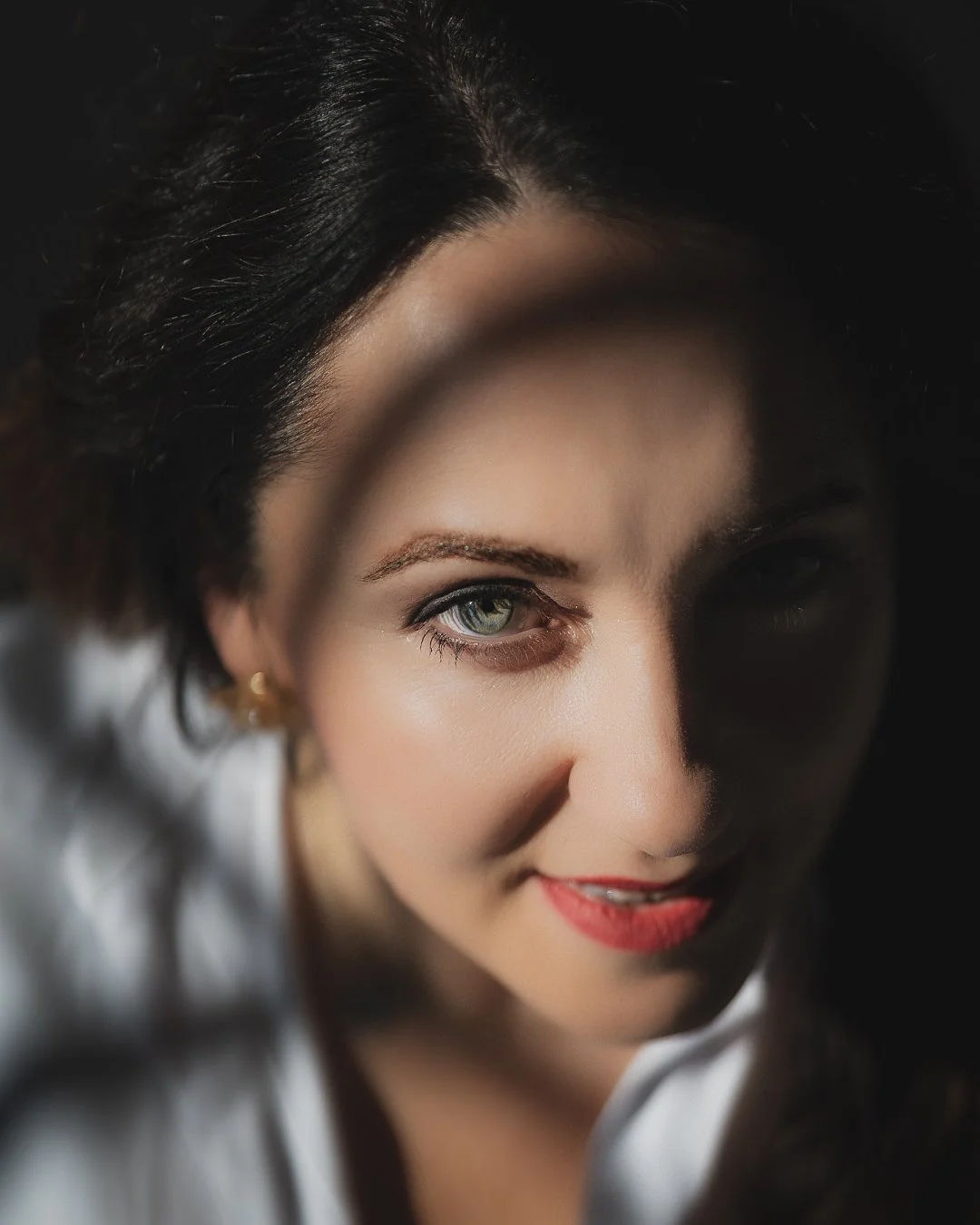 Close-up portrait of a woman with dark hair and blue eyes, smiling at the camera, with one eye partially shadowed.