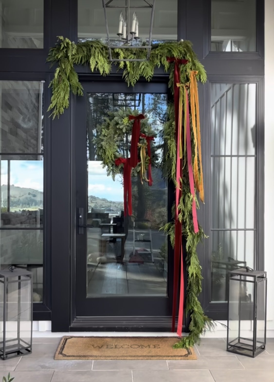 Front door decorated with greenery, red, pink, and orange ribbons, and a welcome mat.