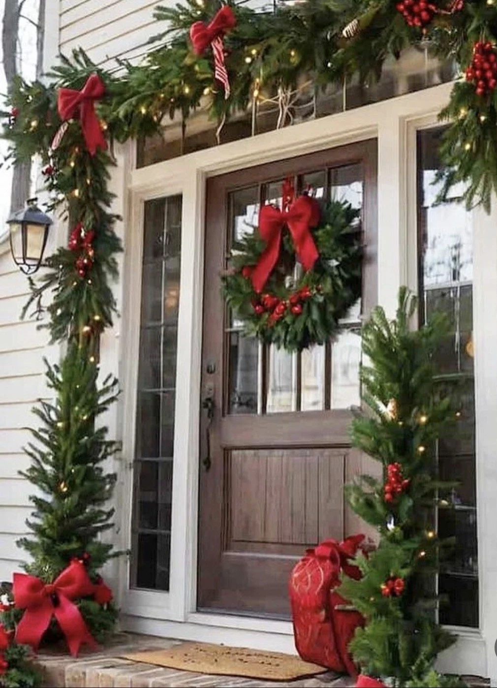 Christmas decorated front door with a festive wreath, red bows, red berries, and string lights.