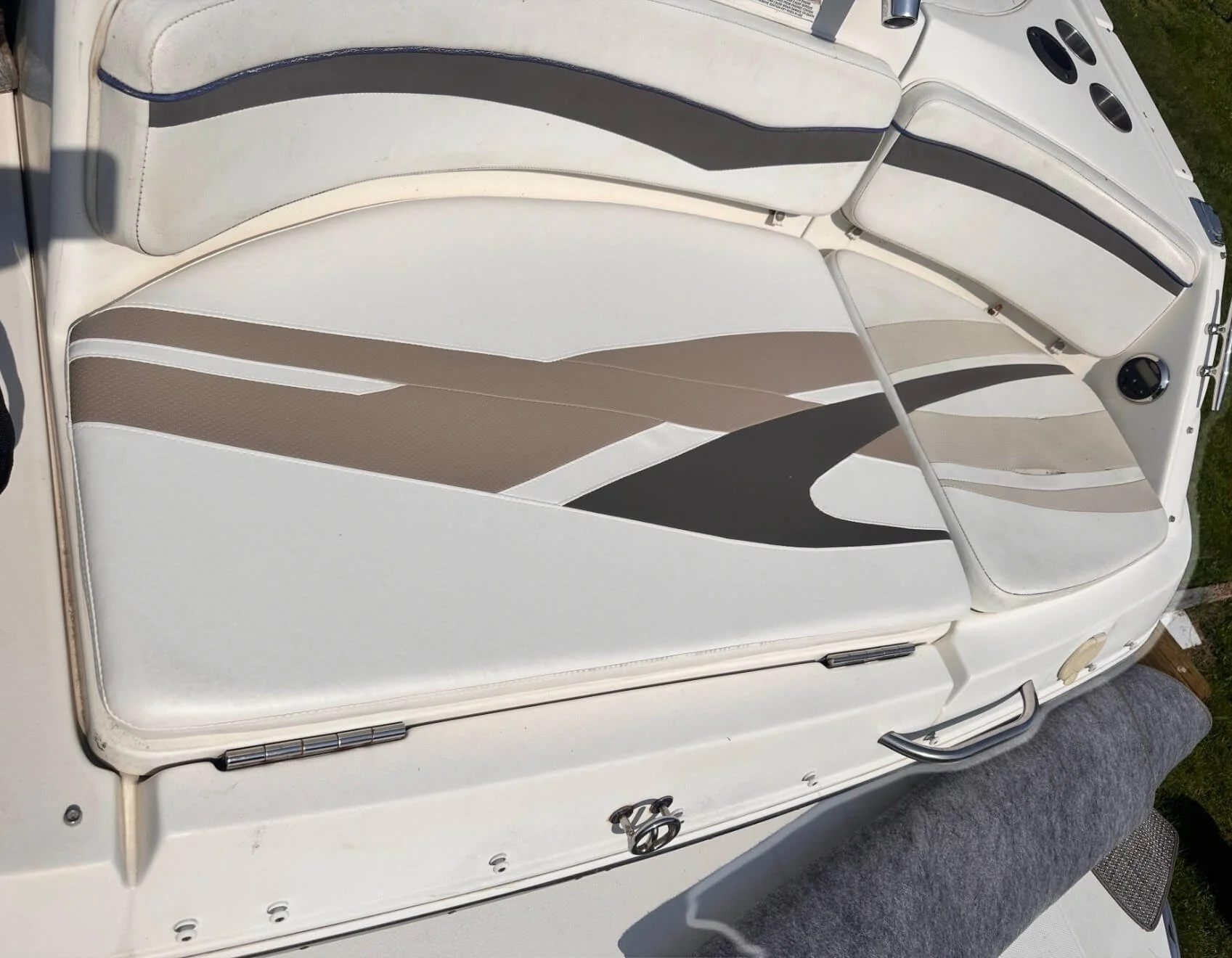The interior of a boat with white and beige cushioned seats with black accents, cup holders, and a metal grab handle, parked outdoors.