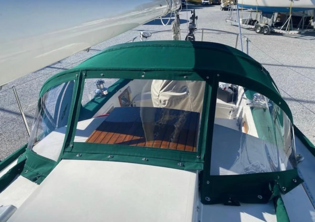 View from above of a boat with a green canopy, transparent side panels, and a wooden deck inside, docked at a marina with other boats in the background.