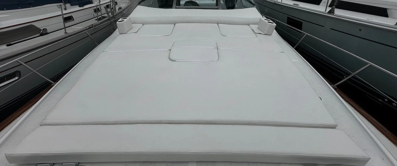 The image shows the top of a white yacht or boat docked between other boats. The surface features hatches and panels, with the water and other boats visible on either side.