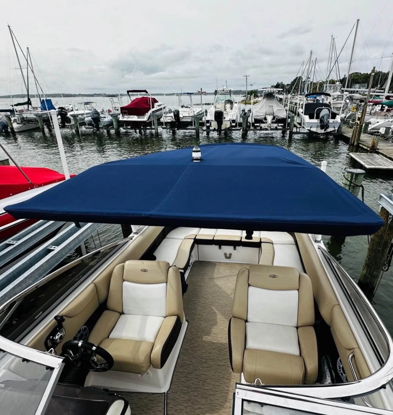 A boat docked at a marina with a navy blue canopy over its passenger area. The interior has beige and white seats, with some boats visible in the background.