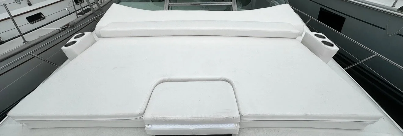 View of a white yacht's front deck with cushions and built-in cup holders, docked among other boats.