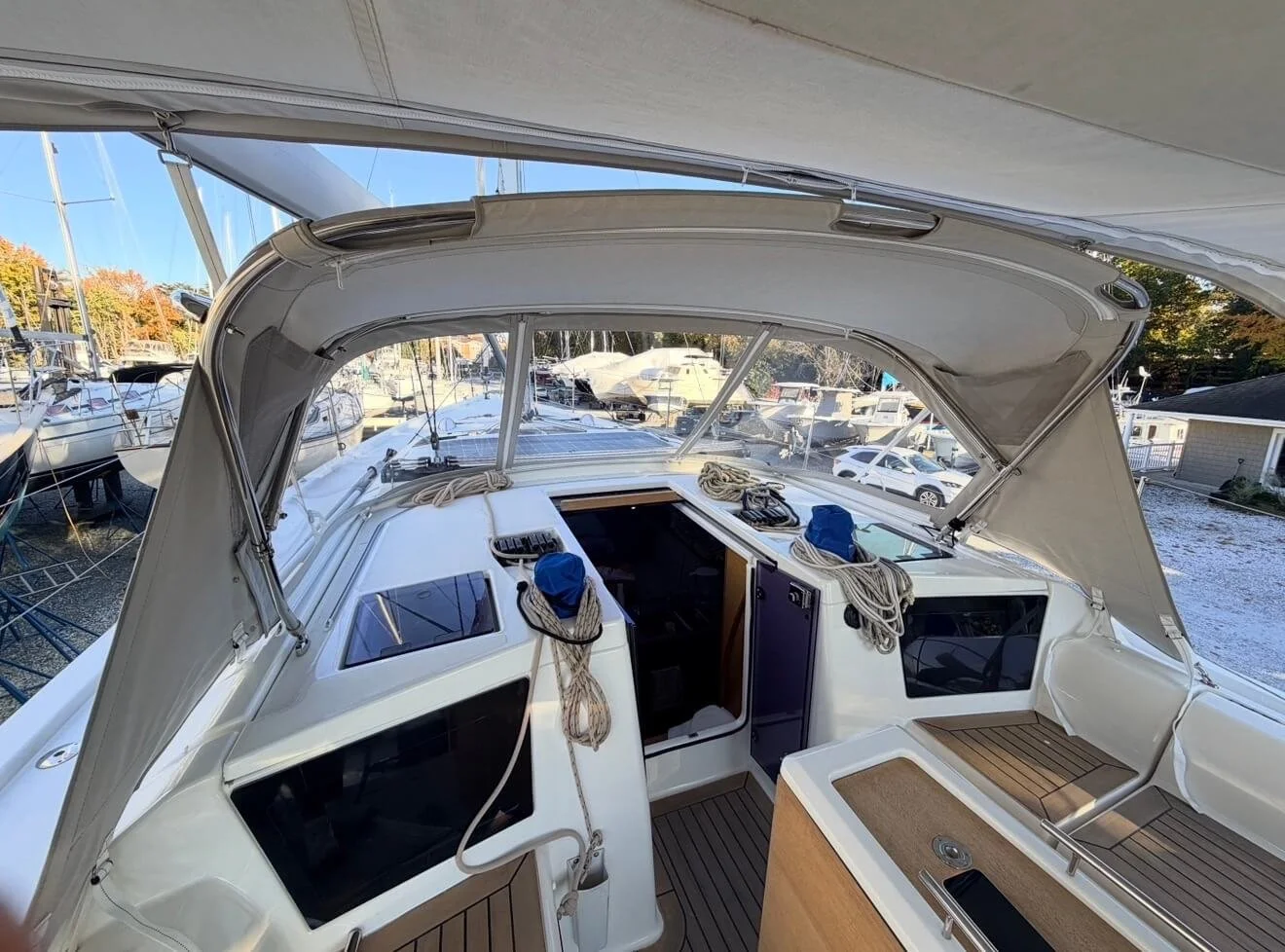 View from the cockpit of a sailboat at a marina, with other boats and trees in the background.