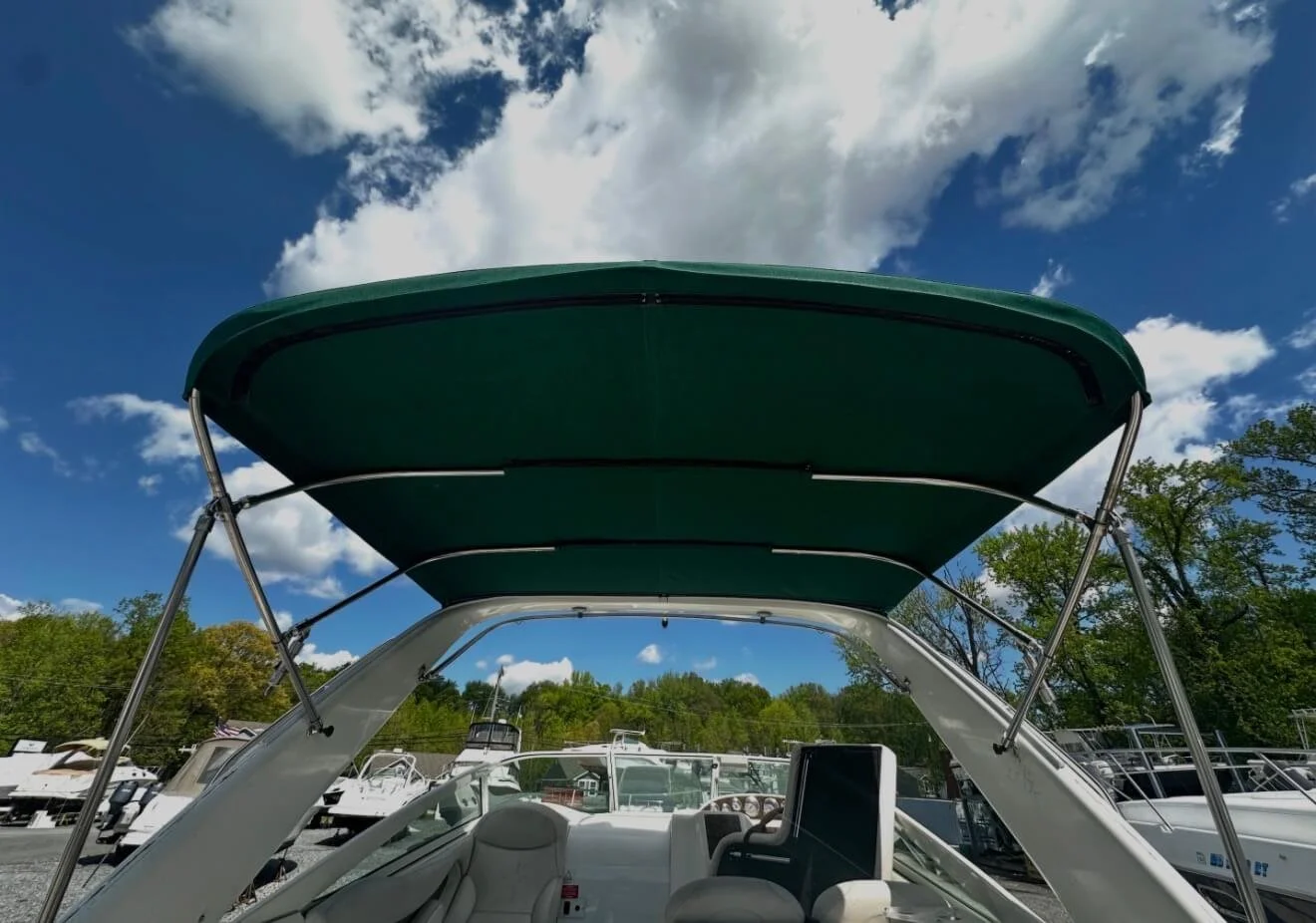 Close-up of a green boat canopy on a yacht at a marina with other boats and trees in the background under a partly cloudy sky.