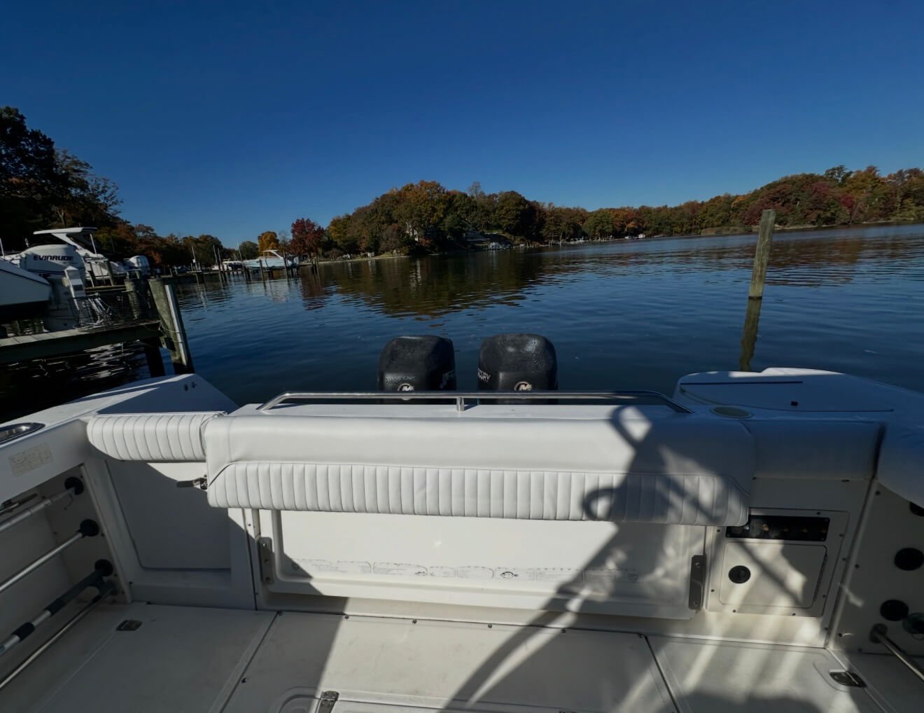 View from a boat on a calm lake with trees in autumn colors in the background, and other boats docked at the marina.