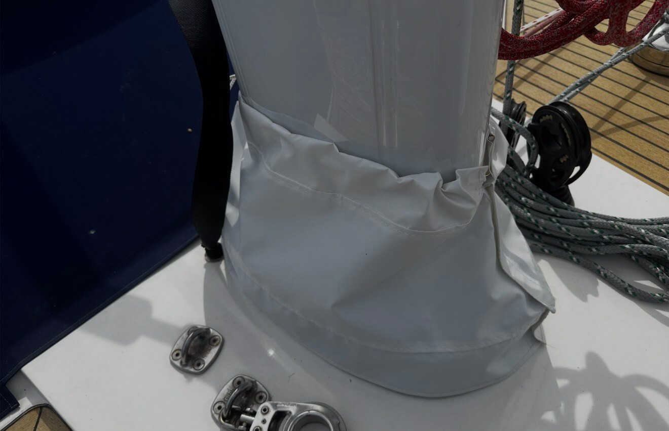 Close-up of a boat's deck showing part of the mast wrapped in a white cover, with a framed metal attachment nearby, and coiled ropes in the background.