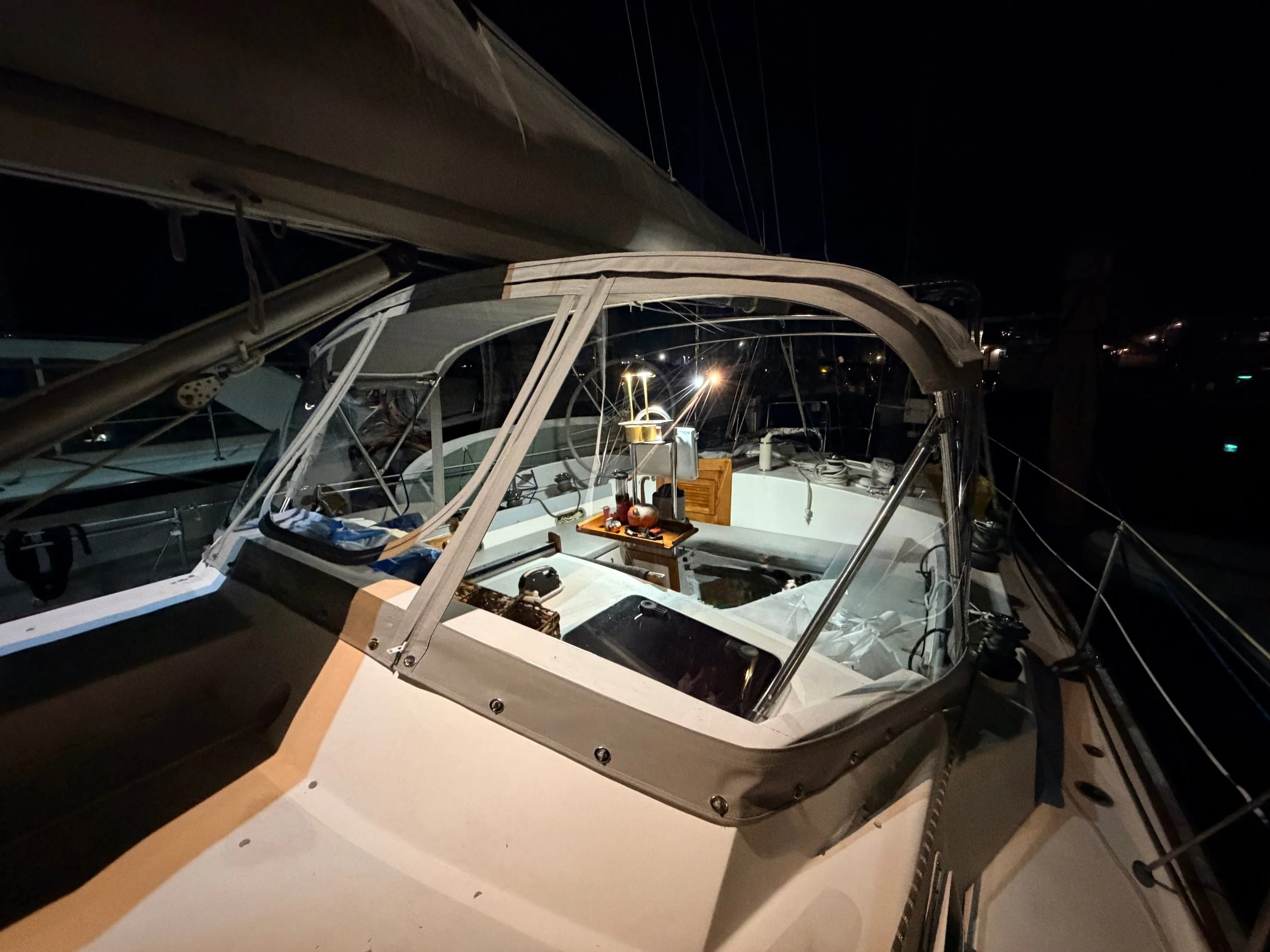 Nighttime view of a sailboat docked at a marina, with interior lights illuminating the cockpit and equipment inside.