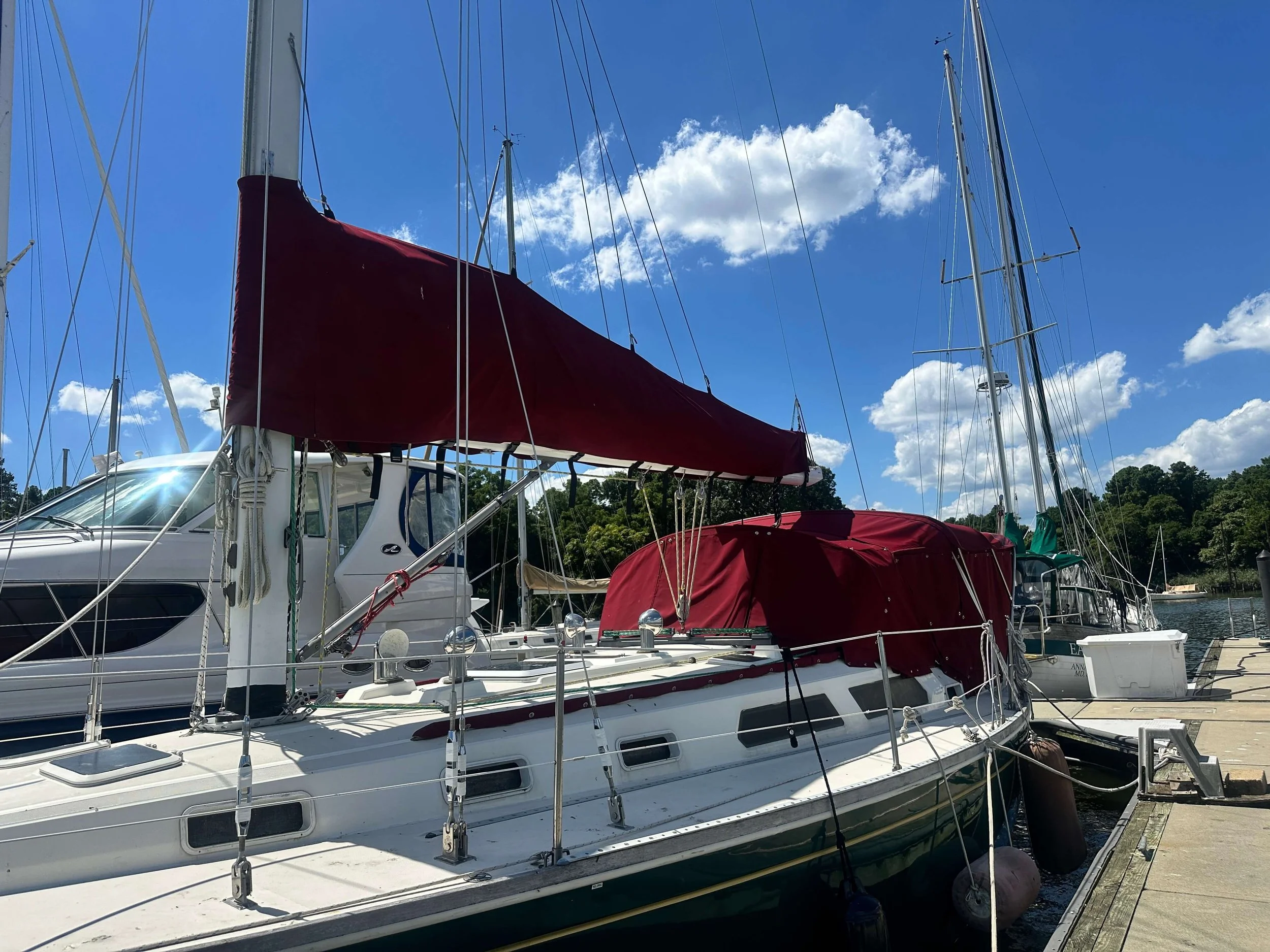 A sailboat docked at a marina with a red sail cover and a blue sky with scattered clouds.