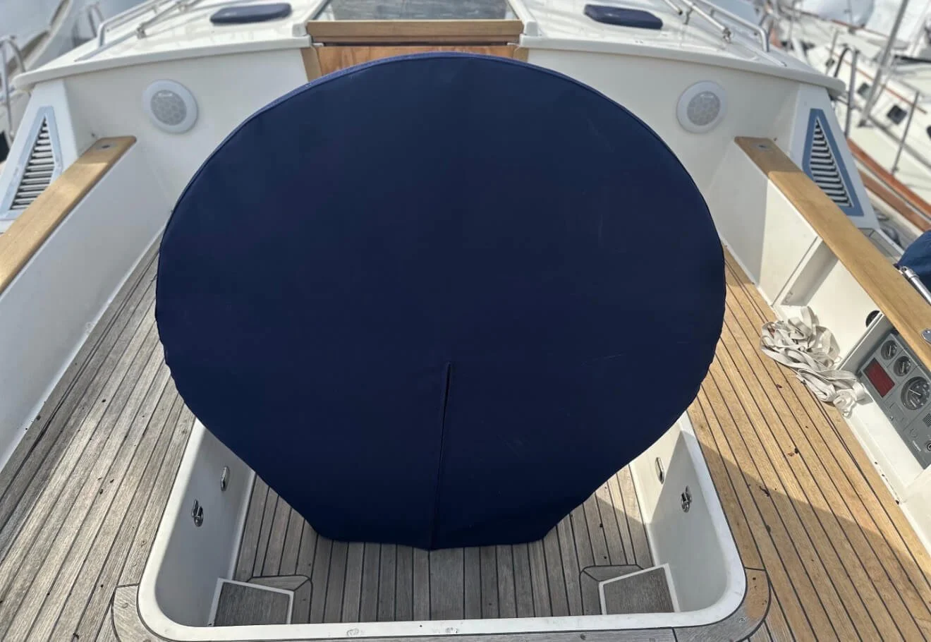 The image shows the deck of a boat with a large, covered object in the center, likely the boat's wheel or navigation area, surrounded by wooden and metal fixtures, with some wires and a pair of gloves on the side.