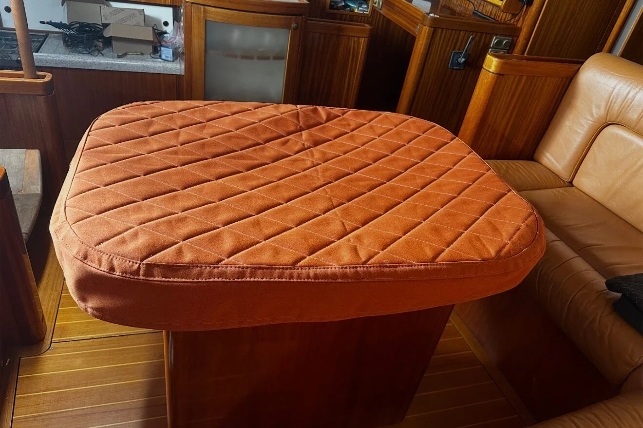 A brown quilted cushioned table or bed on a wooden stand inside a room with wooden walls and floors, next to a tan leather sectional sofa.