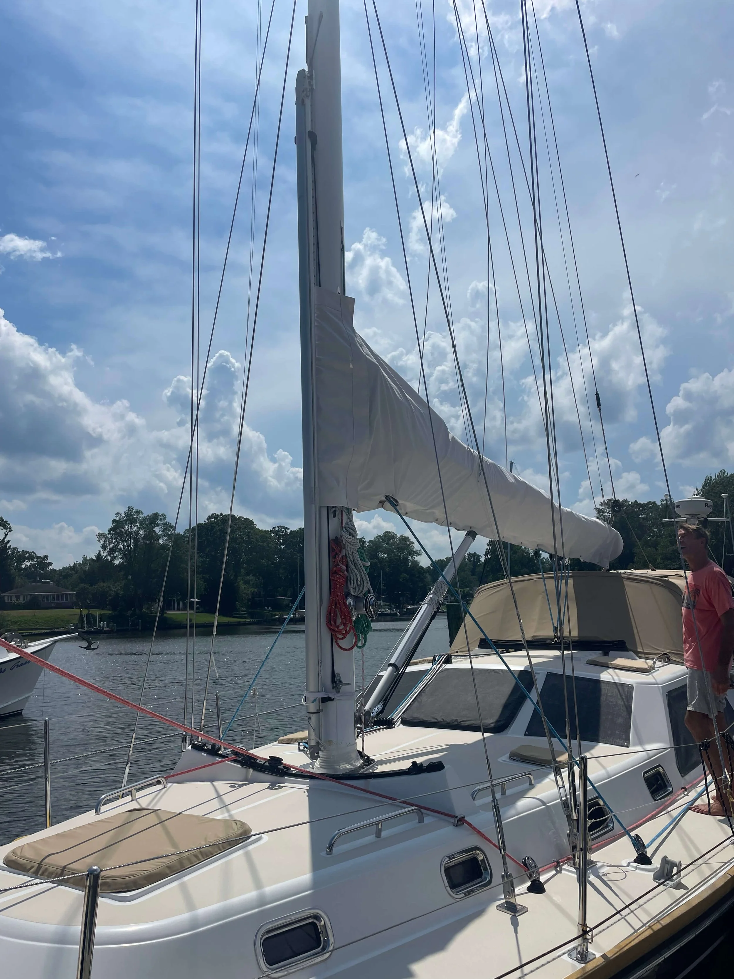 Sailboat docked at a marina on a partly cloudy day, with a man standing on the deck.