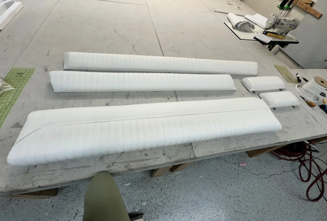 Various white, padded pieces of upholstery fabric laid out on a worktable, with a sewing machine and tools in the background.