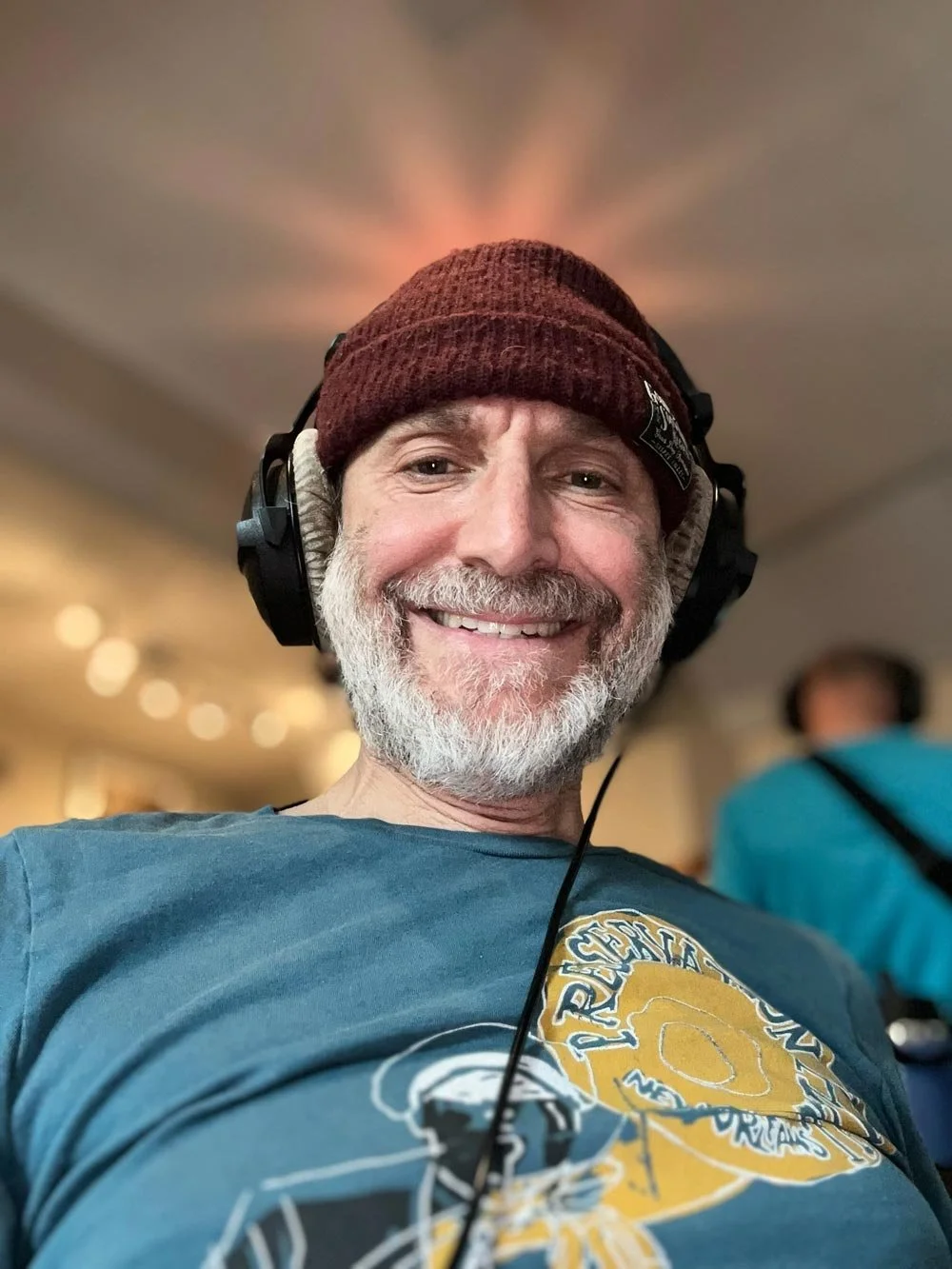 Ben smiling with gray hair and beard wearing a maroon beanie and black headphones.