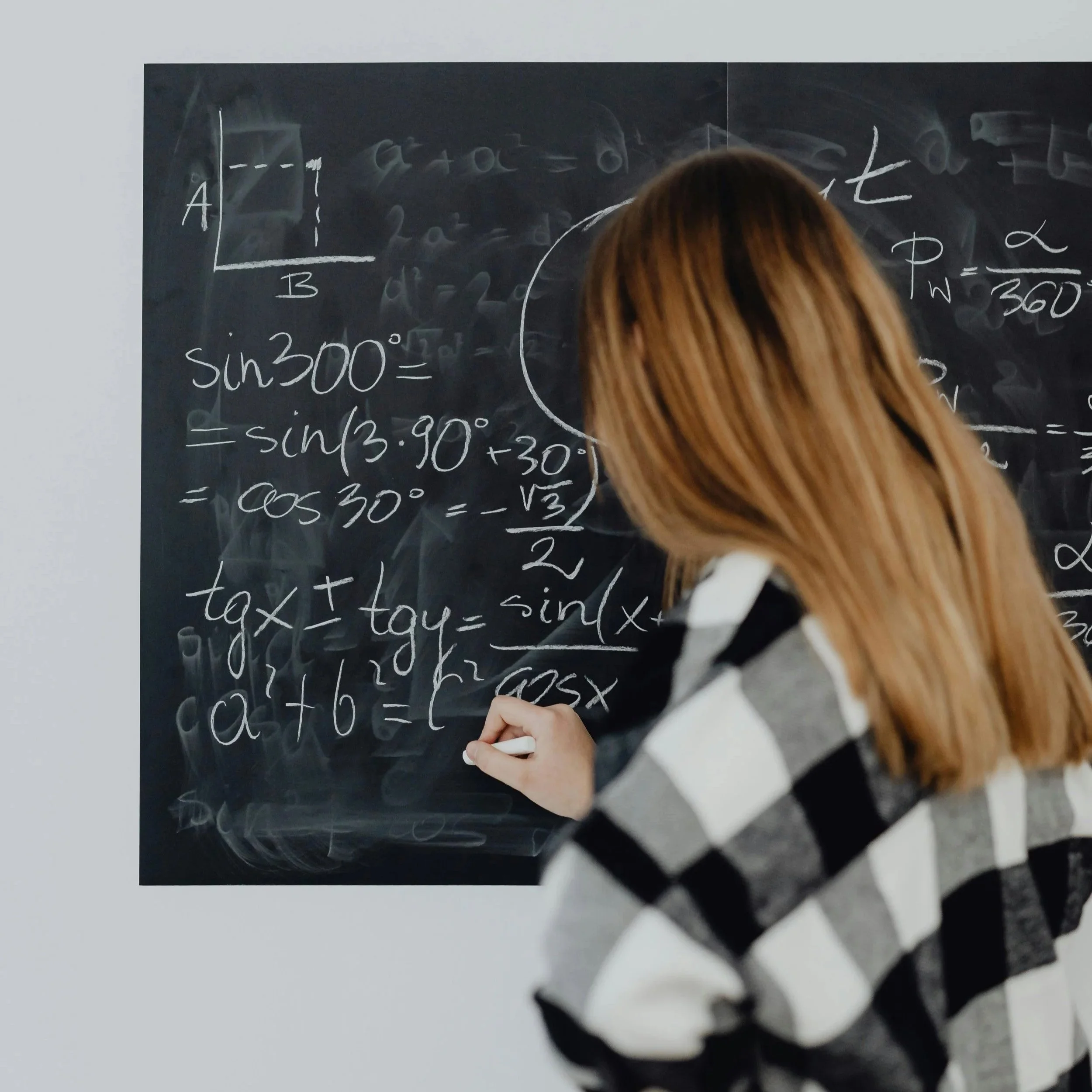 A person with long blonde hair writing mathematical formulas on a chalkboard.
