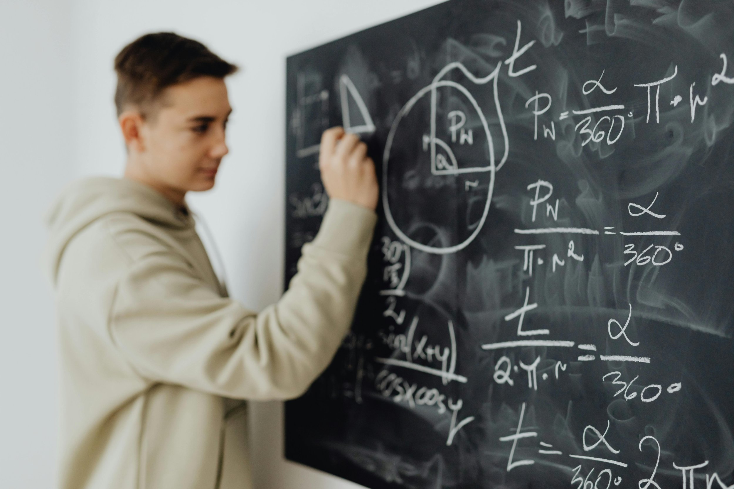 Person writing mathematical equations on a black chalkboard.