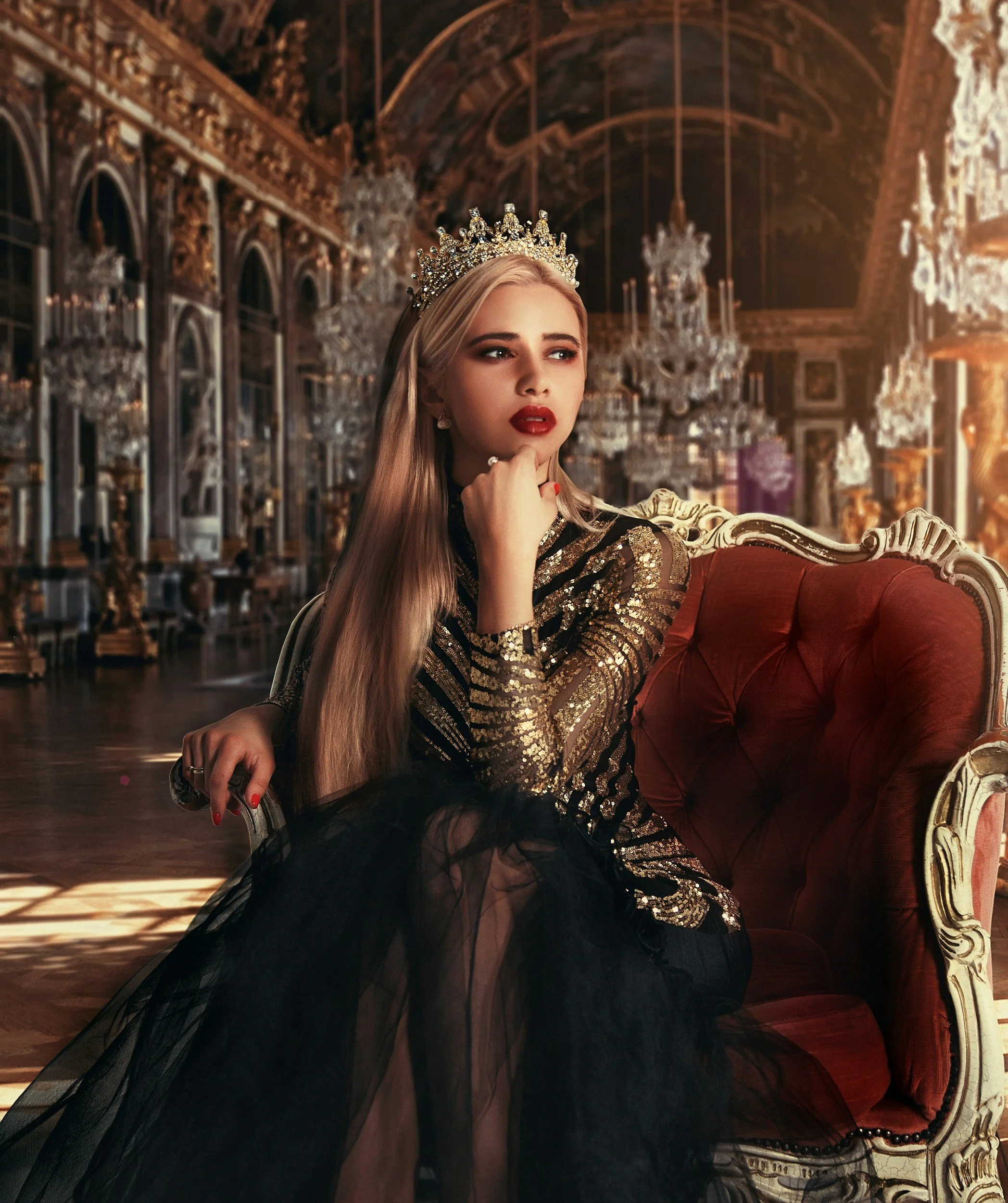 A woman with long blonde hair wearing a crown and a gold sequin dress, sitting on a luxurious red velvet sofa in a grand room with ornate chandeliers and gilded decorations. The Wild Rose Chronicles Membership | Celestial Women's Studies Classes