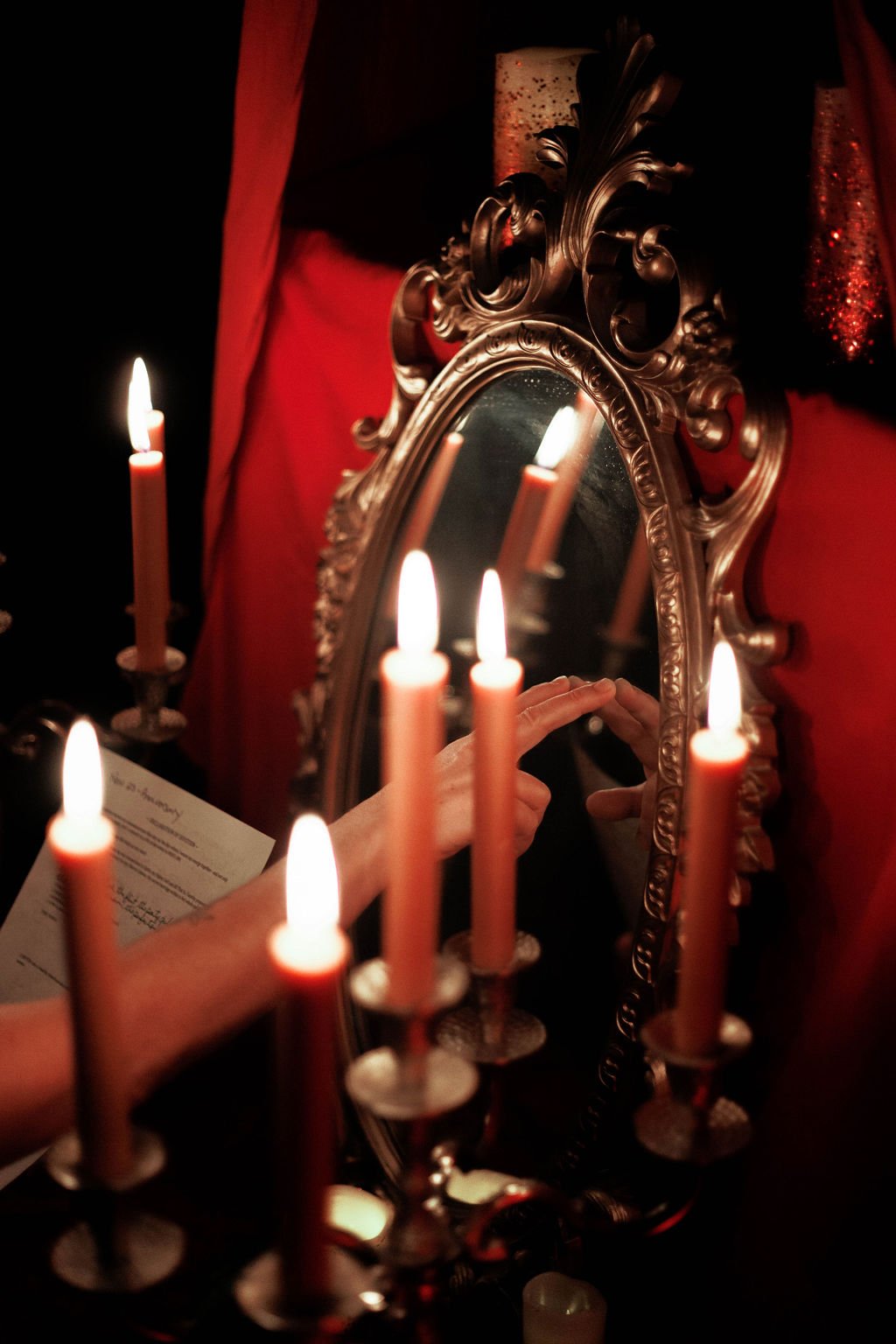 Person lighting candles in front of a decorative mirror with candle reflections, red curtains, and ornate gold frame.