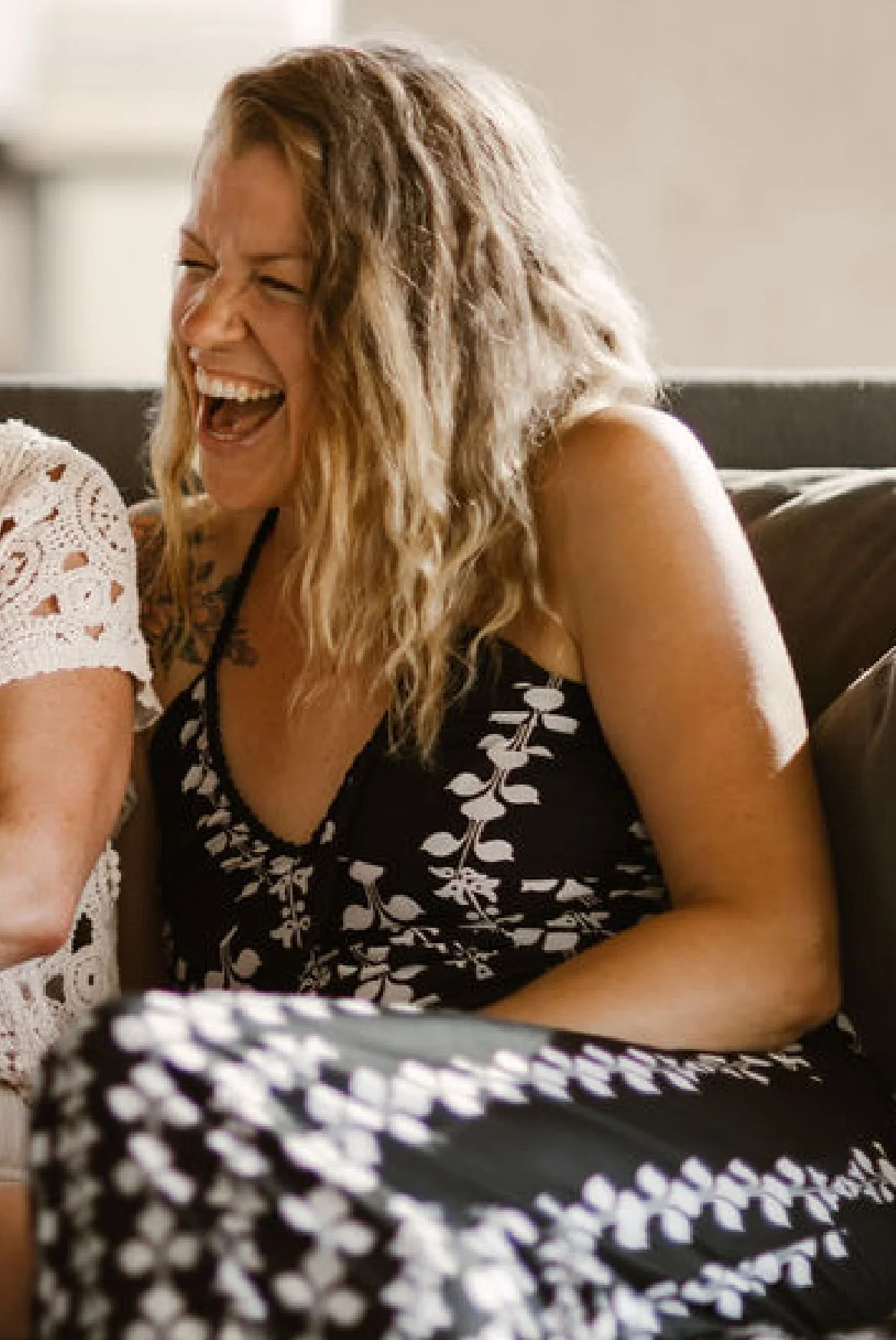 A woman with curly blonde hair laughing in an indoor setting.