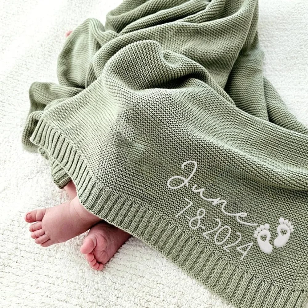 Child's feet sticking out from under a green knitted blanket with personalized embroidery and a flower design on the corner.
