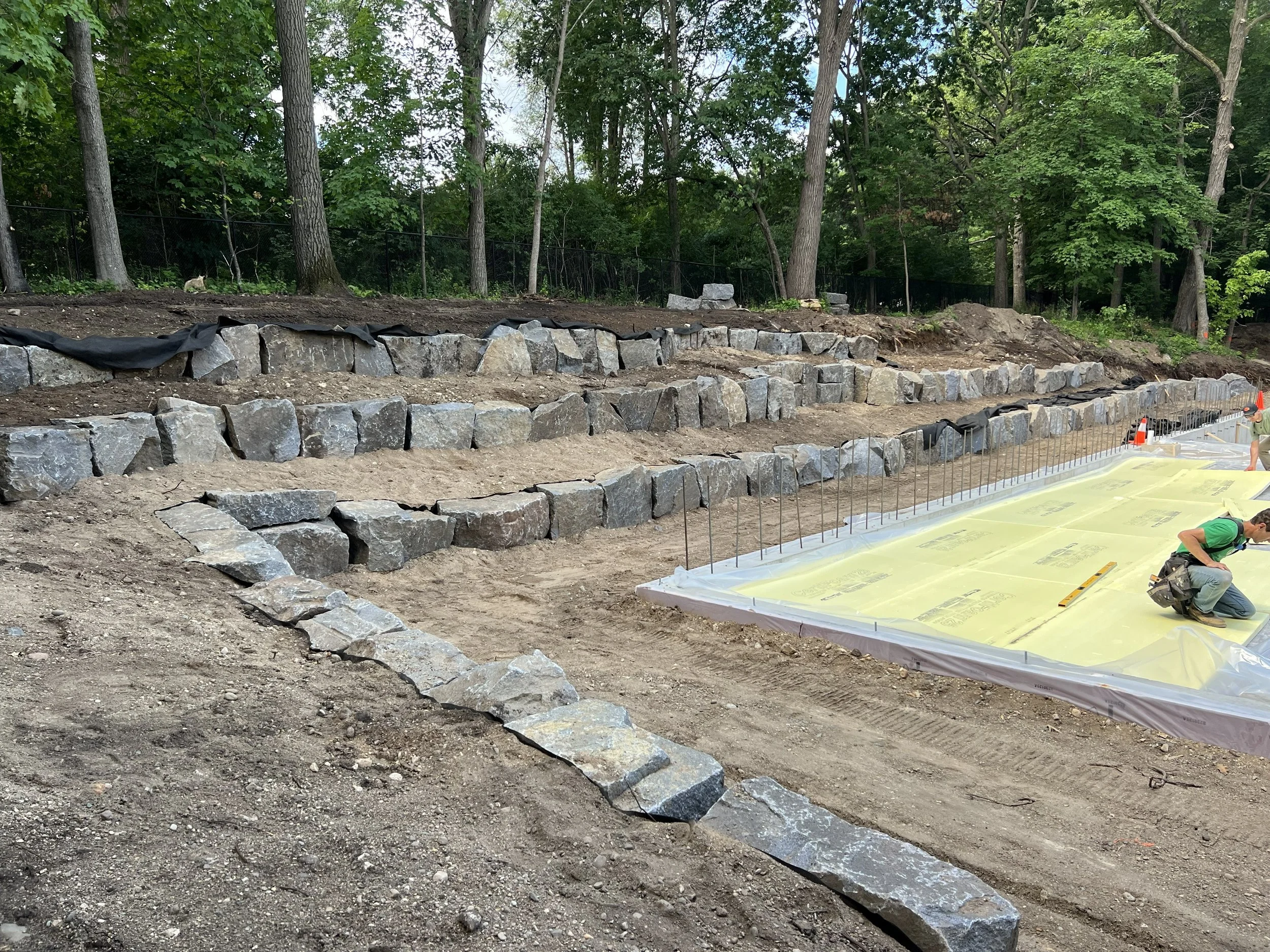 Construction site with unfinished stone staircase and workers installing insulation sheets in the foreground.
