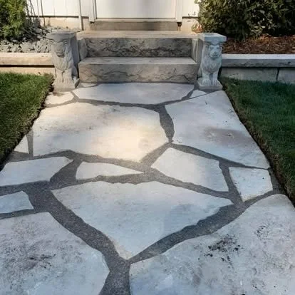 Cracked and uneven concrete walkway with decorative stone steps at the entrance of a house.