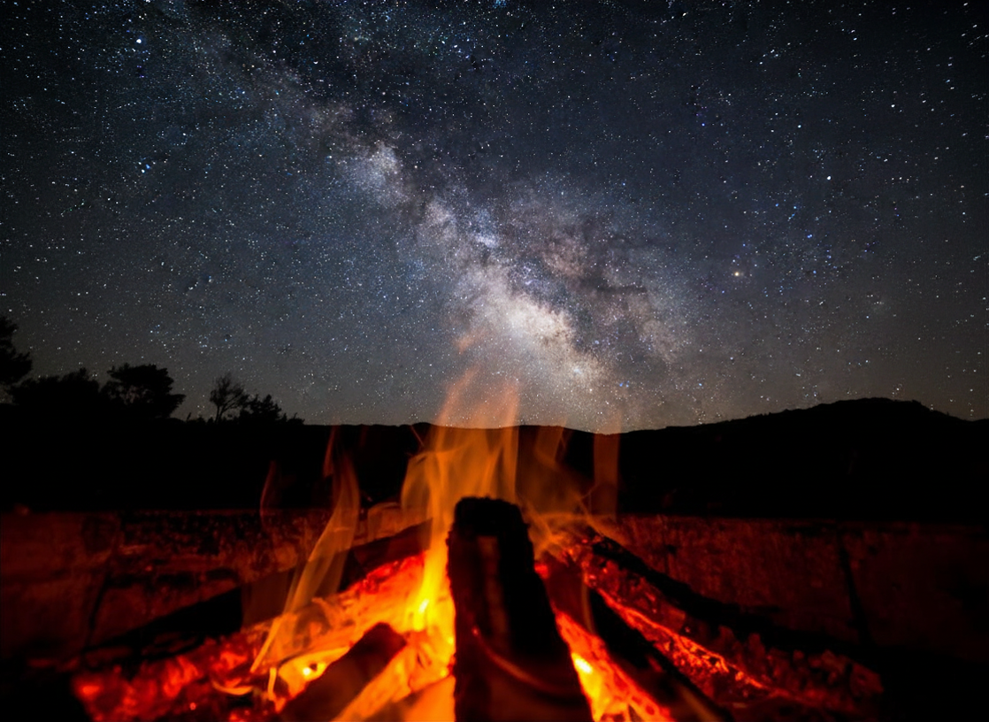 Campfire embers with a nighttime silhouette of a state park, and spectacular stars overhead.above