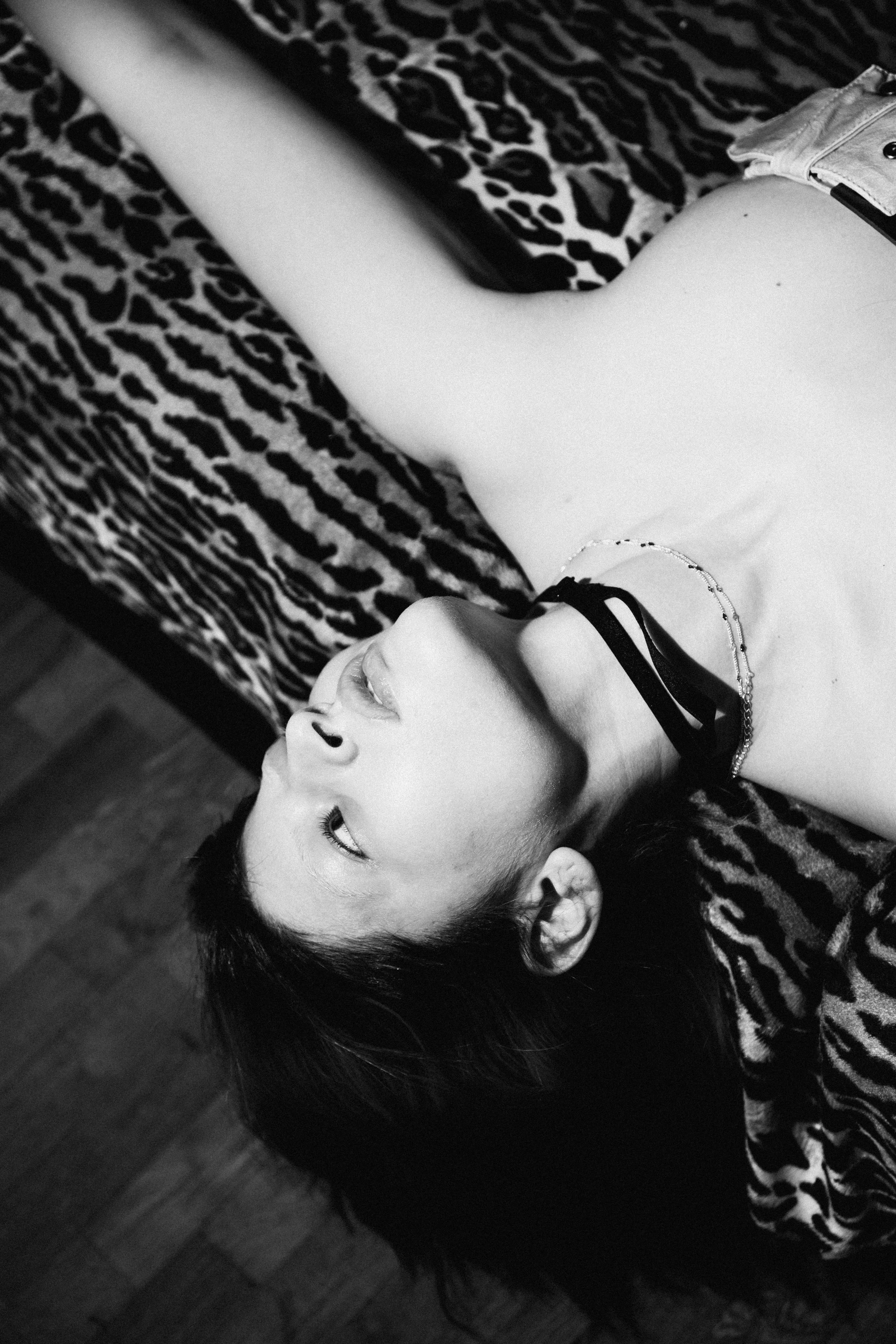 A young woman with short dark hair lying on a leopard-print blanket on a wooden floor, looking to the side.