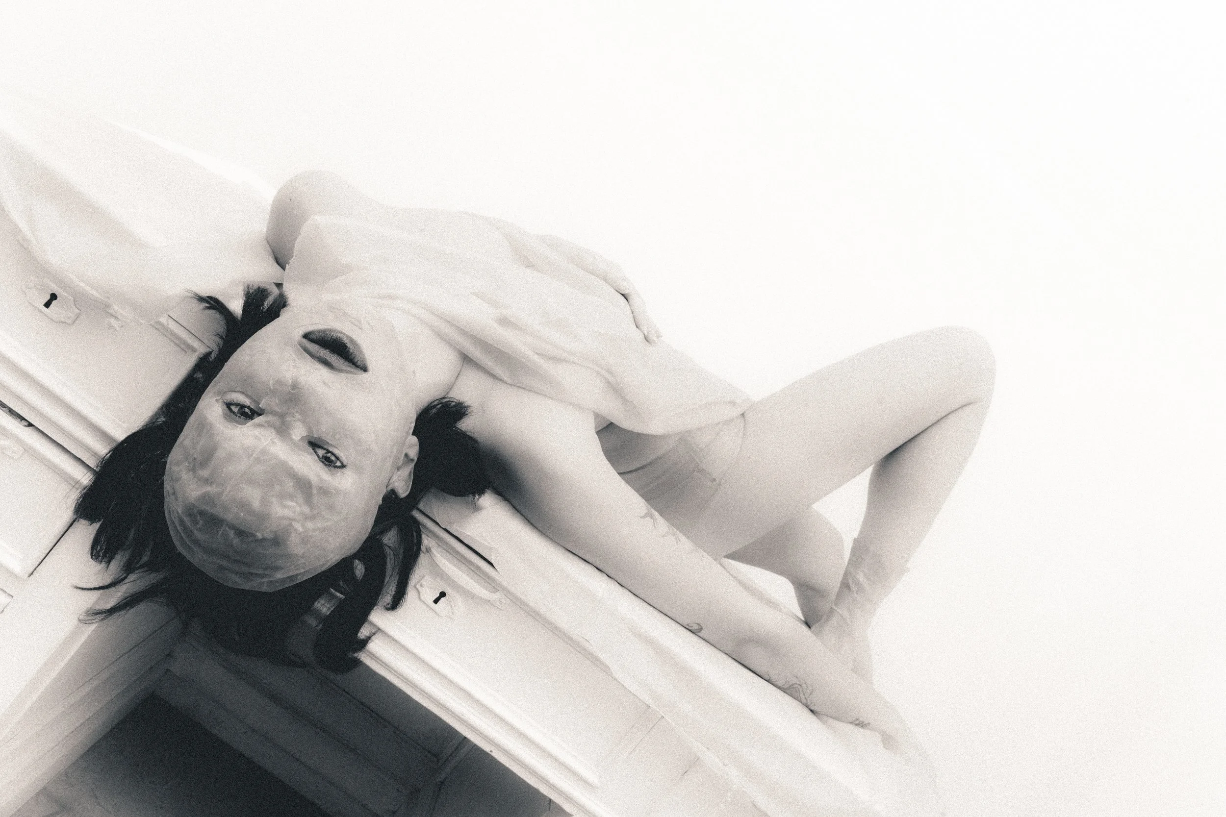 A woman with wet hair lying on top of a cabinet in a bathroom, wearing a towel and looking up at the camera.