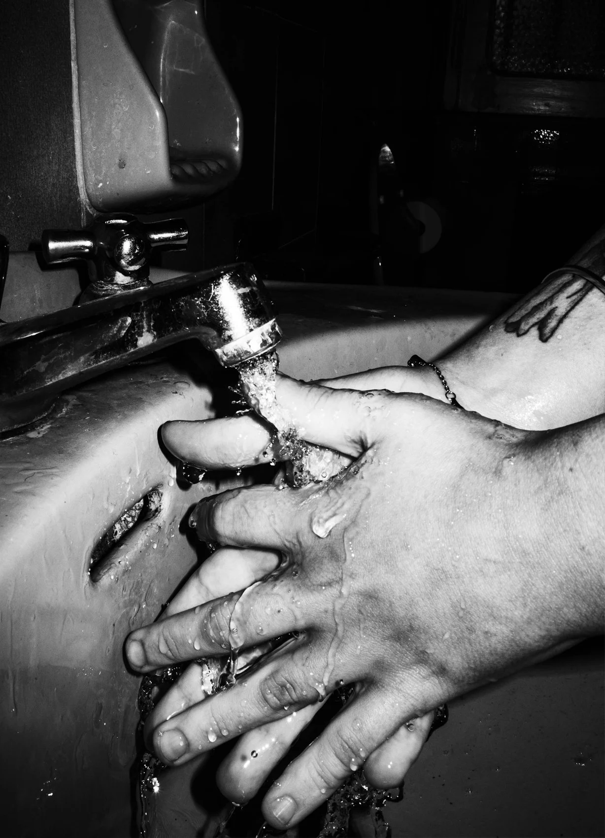 Two hands washing under a running faucet in a sink, in black and white.
