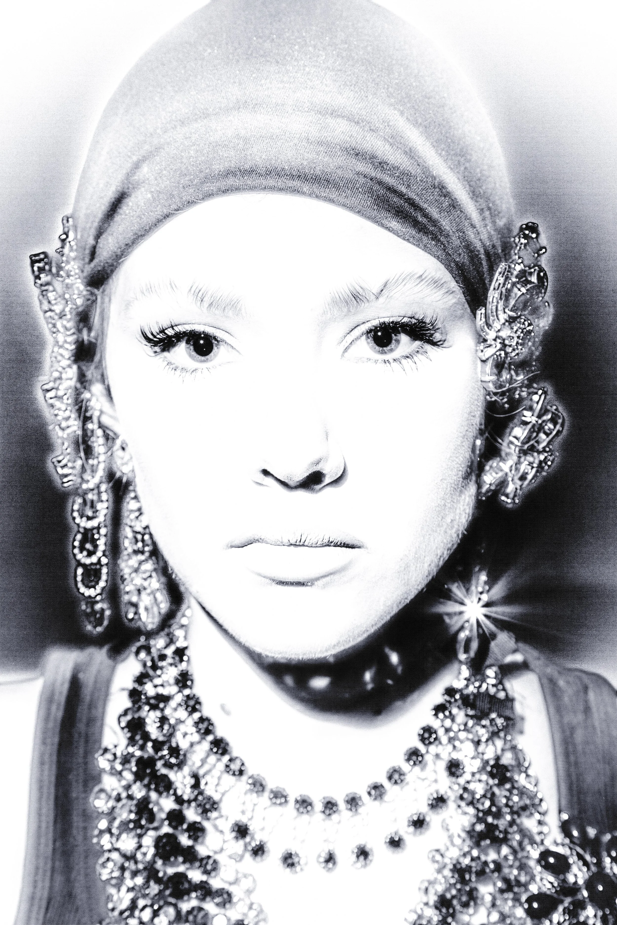 A black-and-white portrait of a woman wearing a headscarf and elaborate jewelry, including earrings and necklaces.