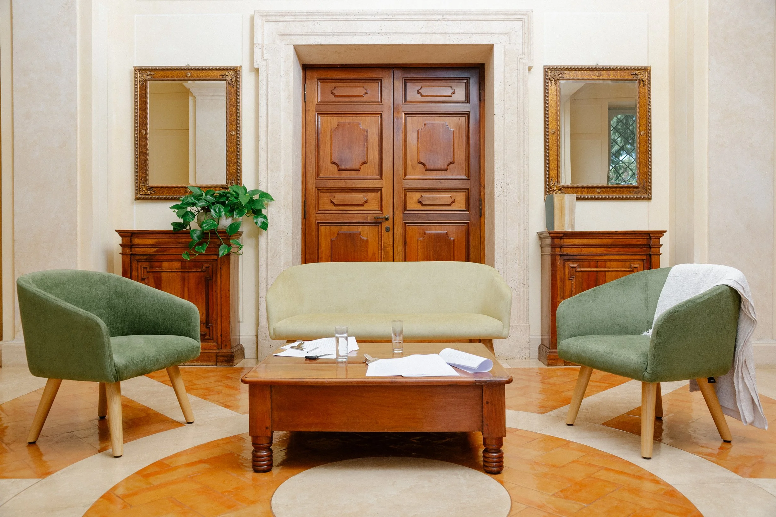 Living room with green and beige furniture, wooden door, two mirrors, and wooden side tables.