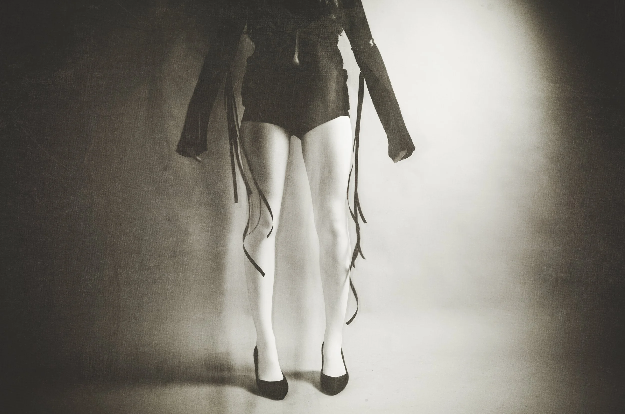 A mannequin wearing black high heels, black shorts, and a black jacket with long sleeves, with black ribbons hanging from the jacket.