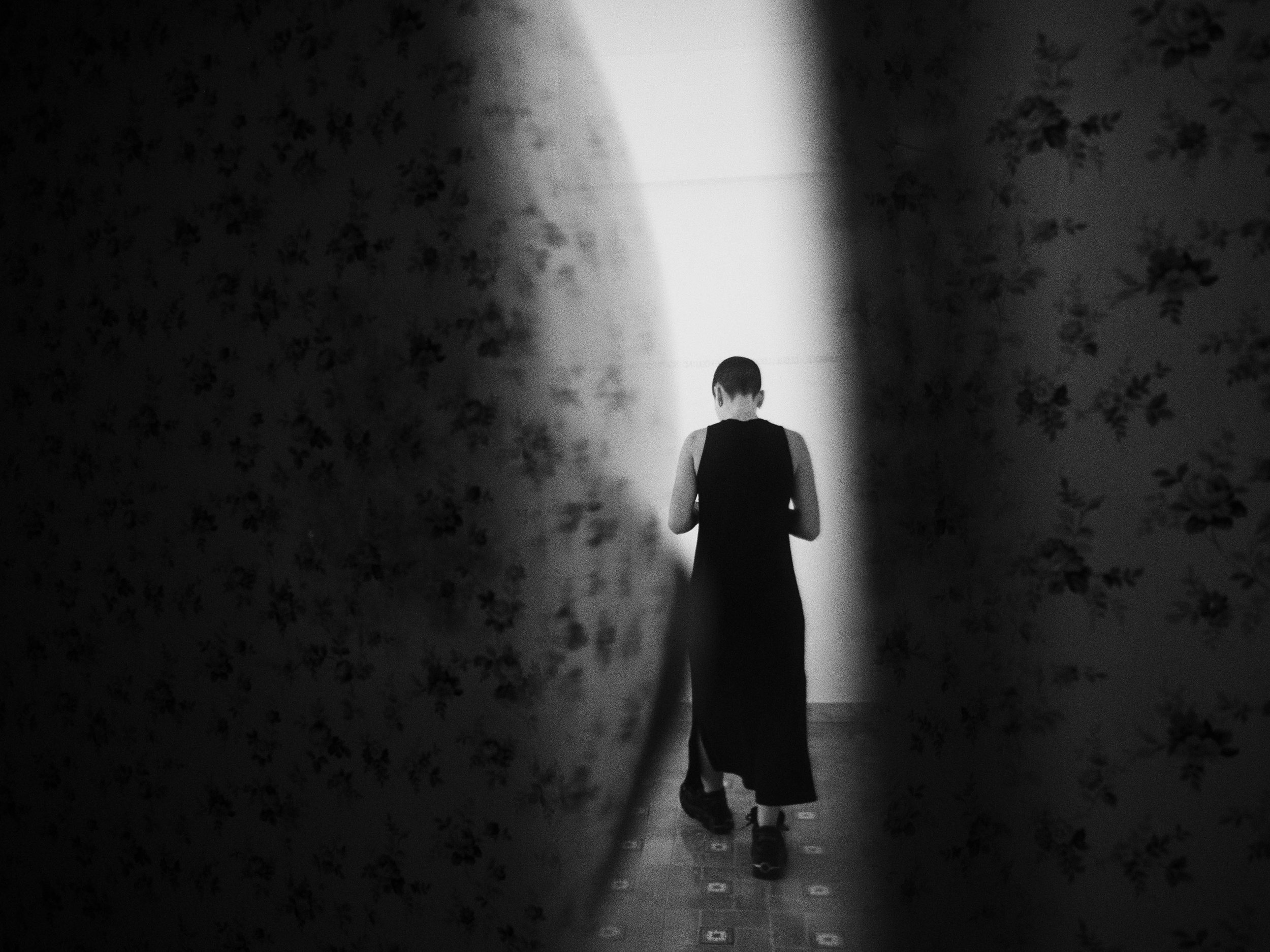 A person walking away in a corridor, viewed through a curtain with a floral pattern.
