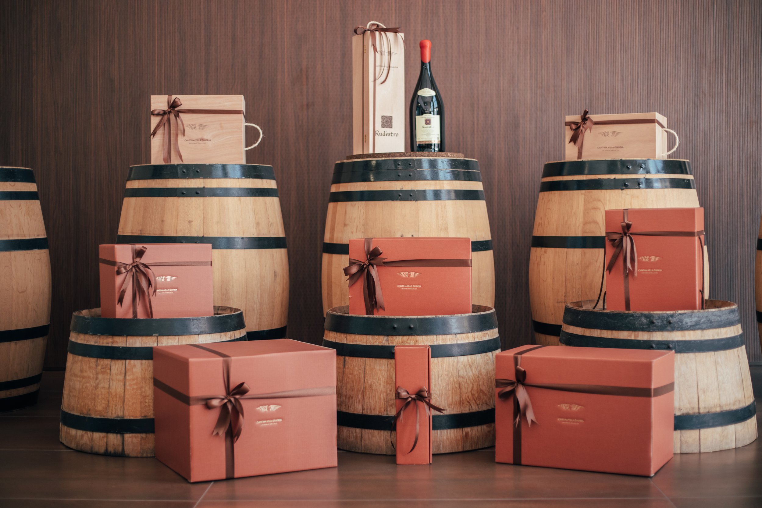 Decorative wooden wine barrels with gift boxes on top and around them, a bottle of wine on a barrel in the center