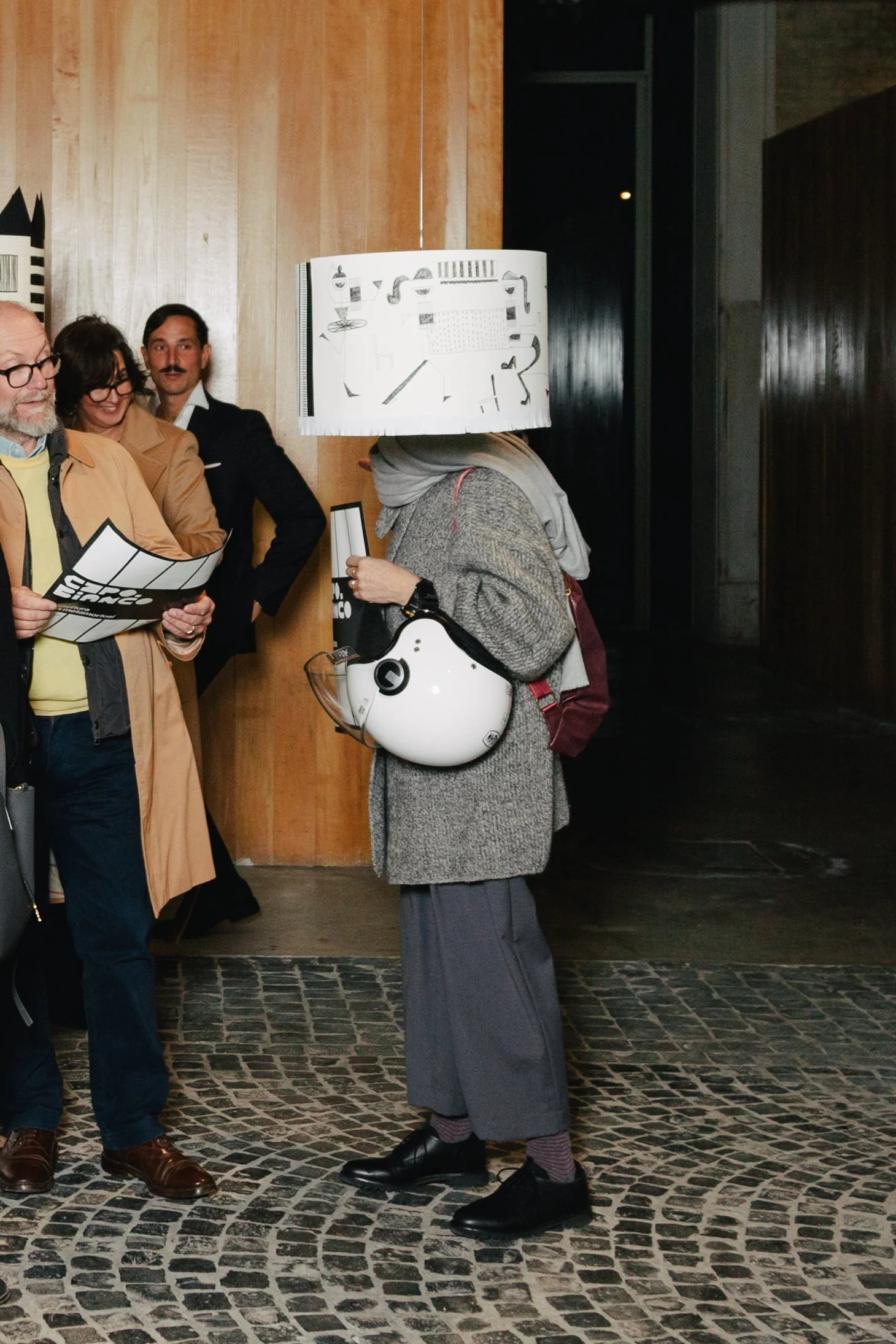 Person with a lamp and helmet costume standing among a group of people indoors.