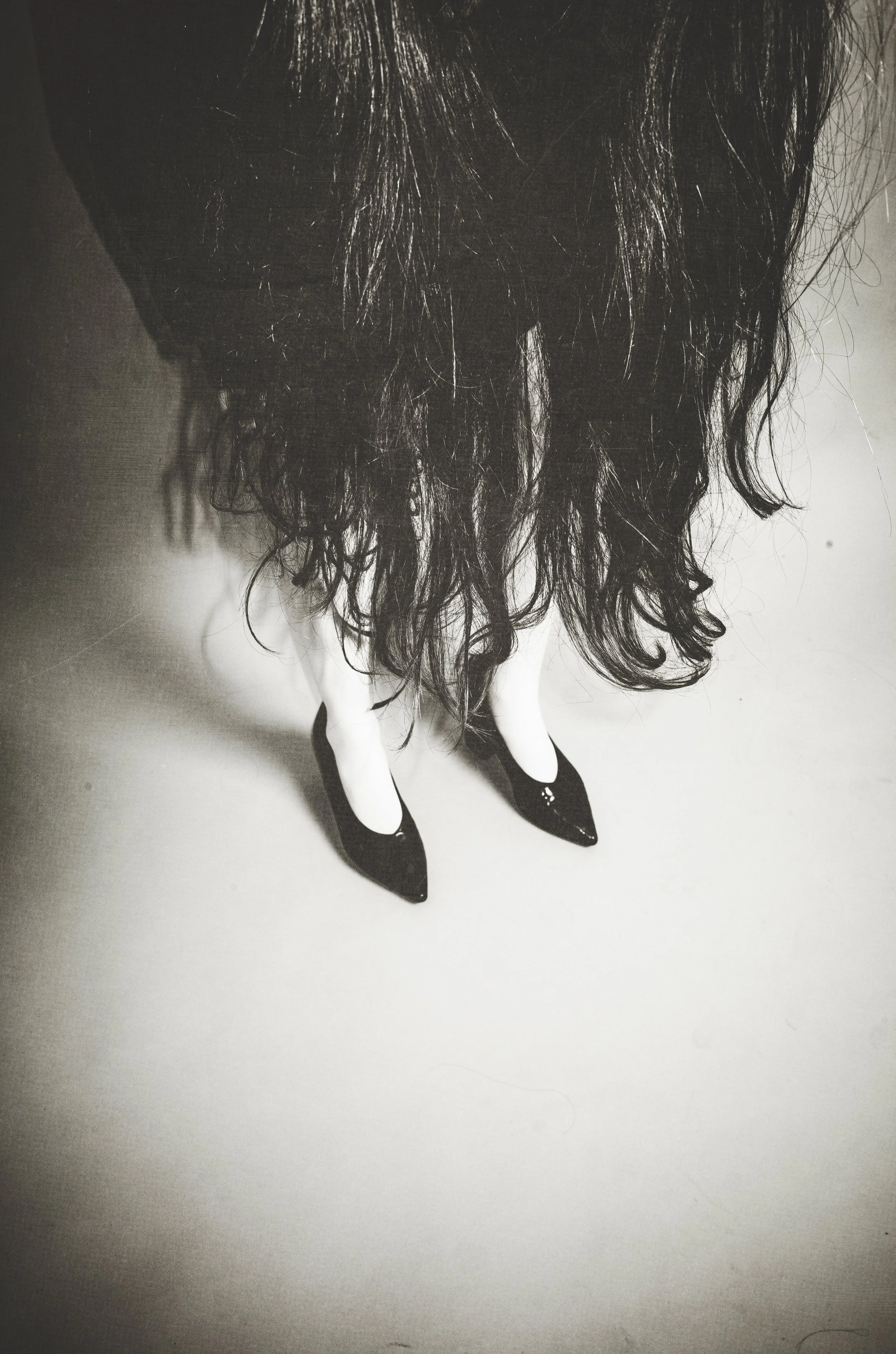 Black high-heeled shoes with white accents worn by a person with long, curly dark hair, seen from above.