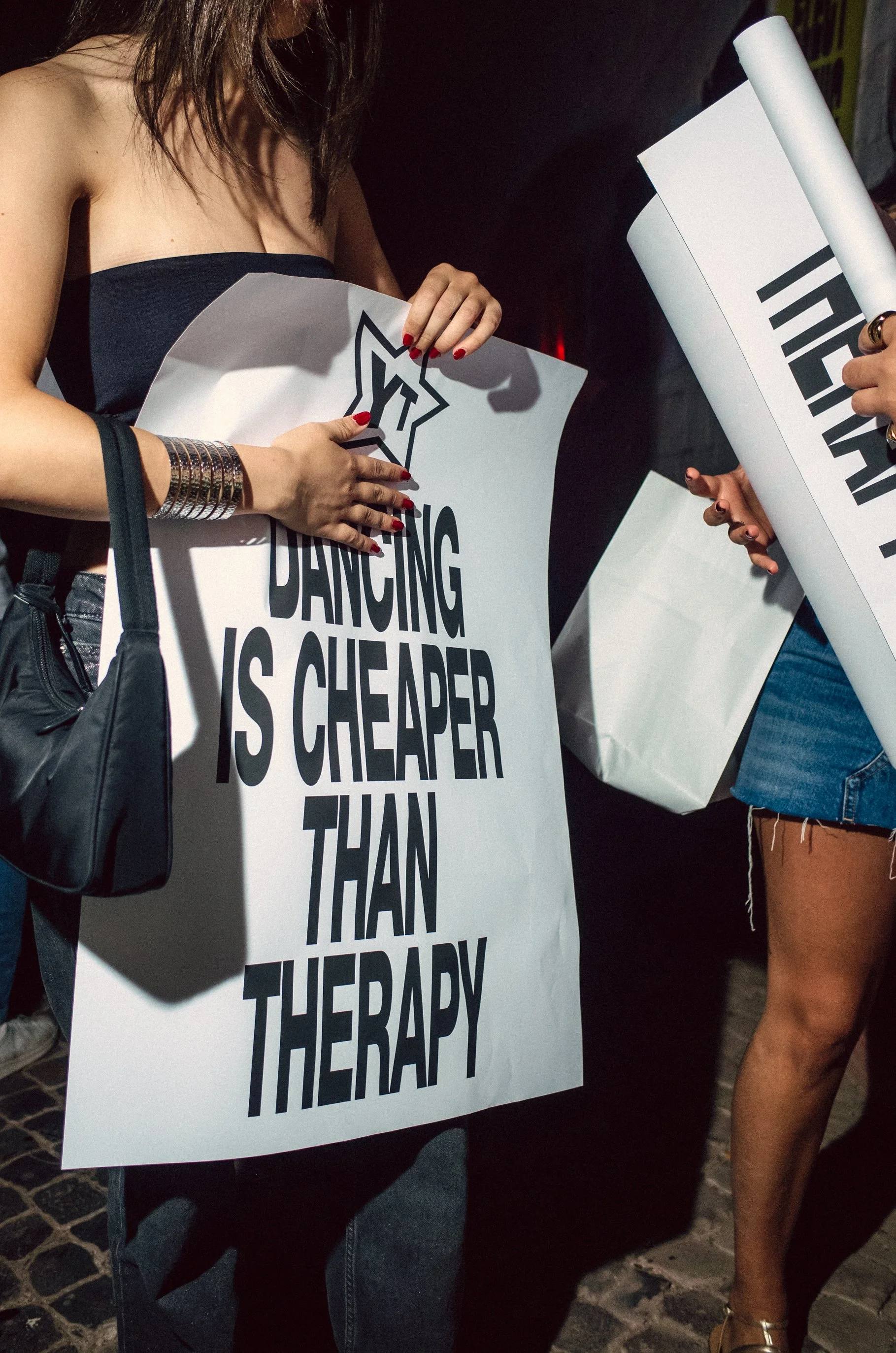 People holding signs at a protest, with one sign reading 'Dancing is cheaper than therapy'