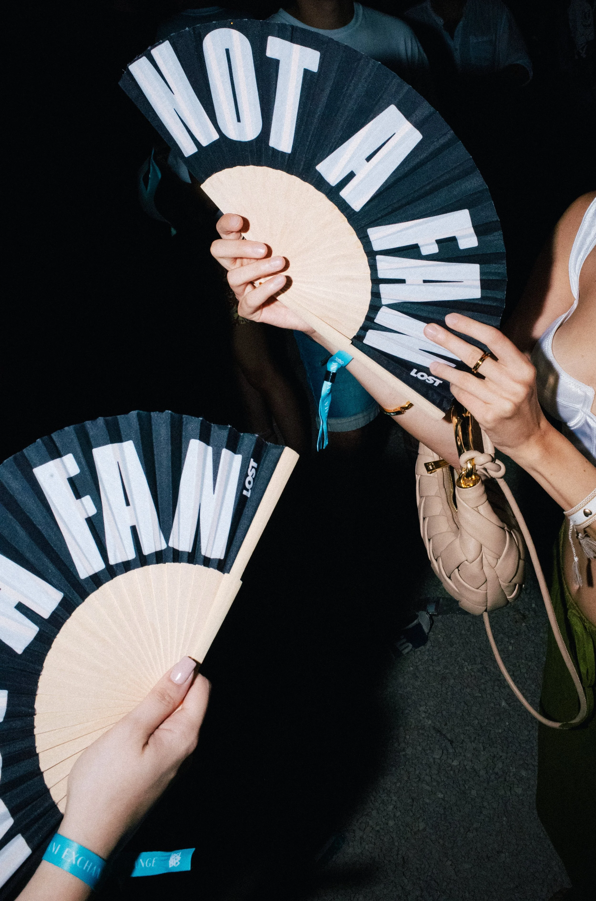 People holding fans that say 'DO NOT FAWN' and part of one fan that says 'STAY FAM' in a dark setting.
