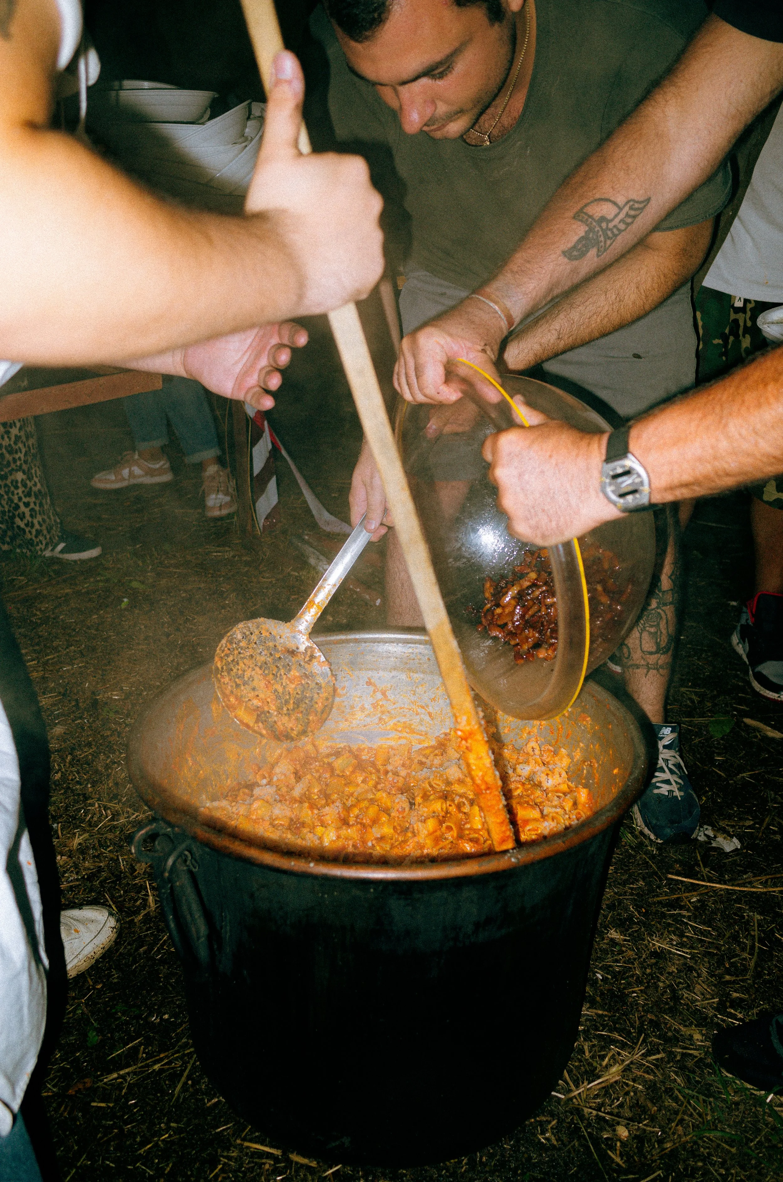 People preparing a large pot of chili at an outdoor gathering.