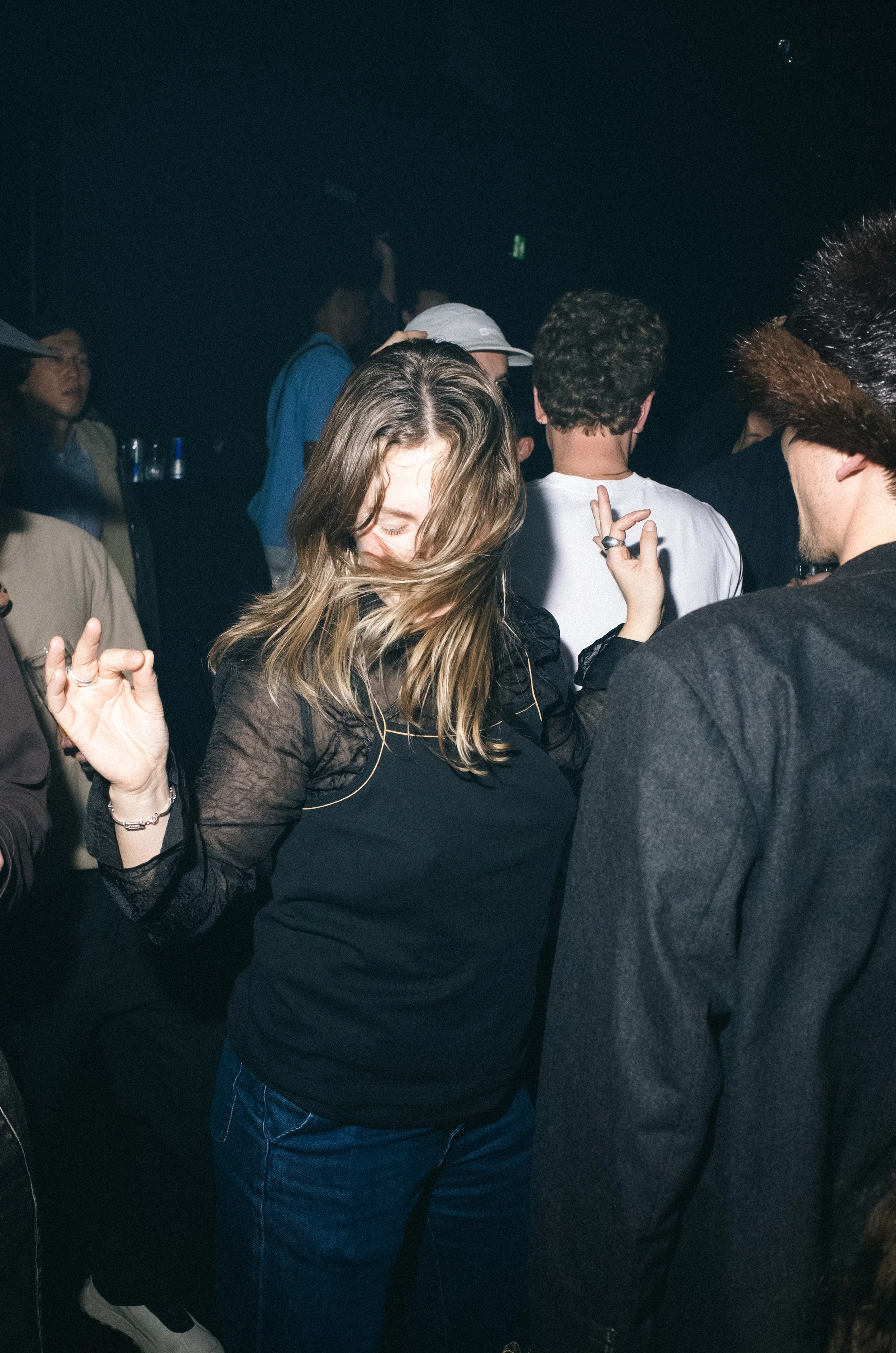 A group of people dancing in a dark, crowded nightclub or party setting.