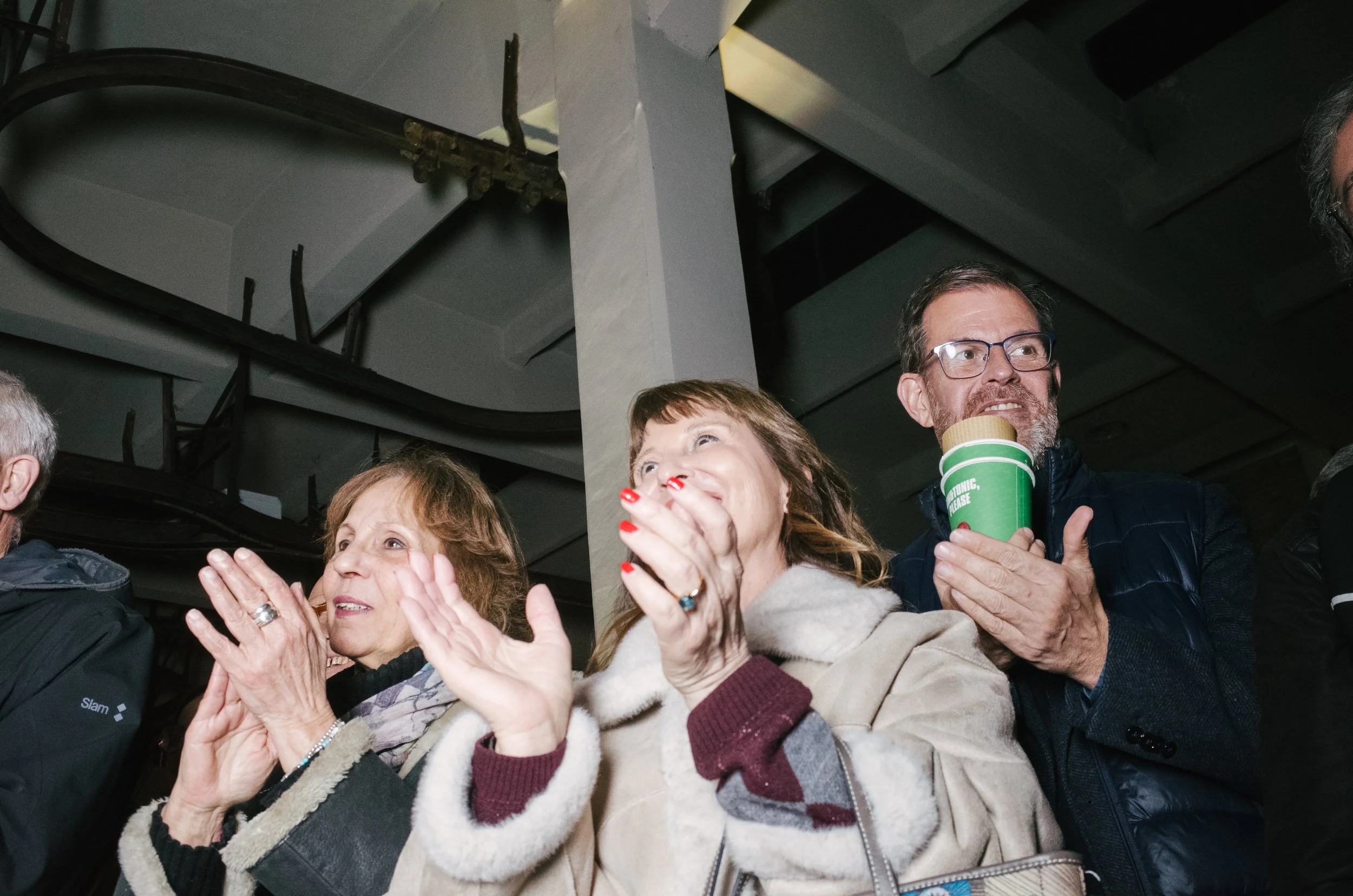 Group of people clapping and watching an event, with some smiling.