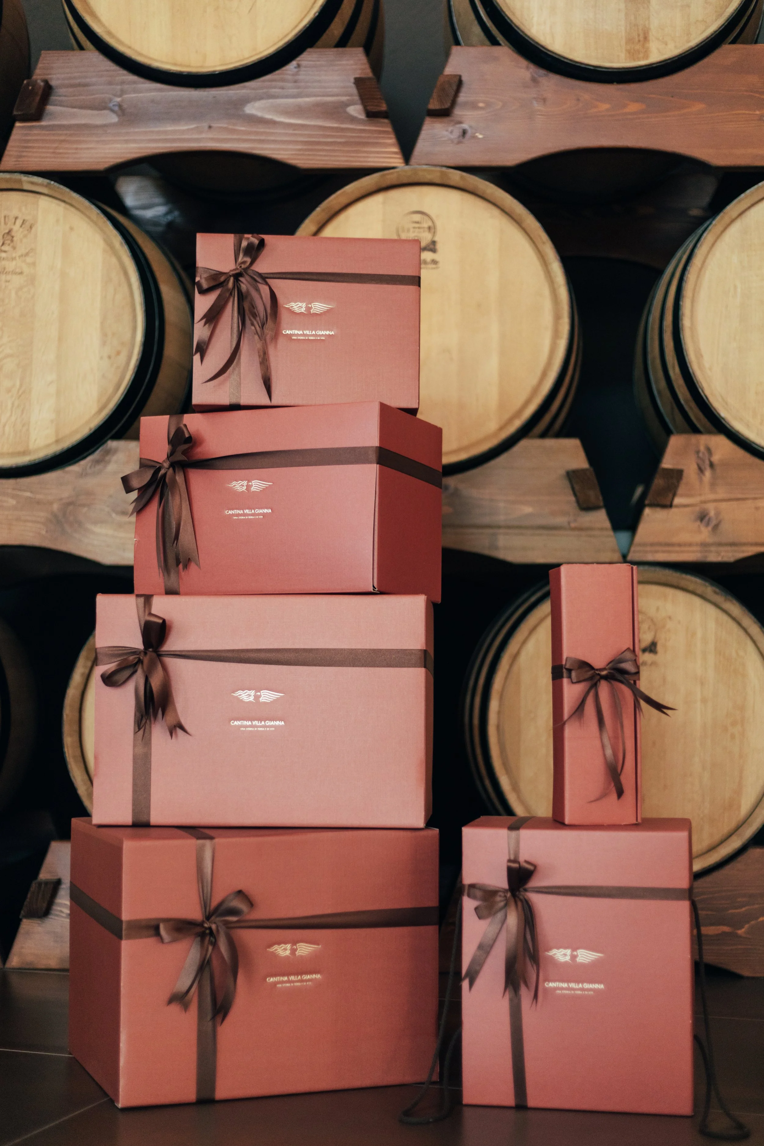 Stacked pink gift boxes with brown ribbons in front of wine barrels in a cellar.